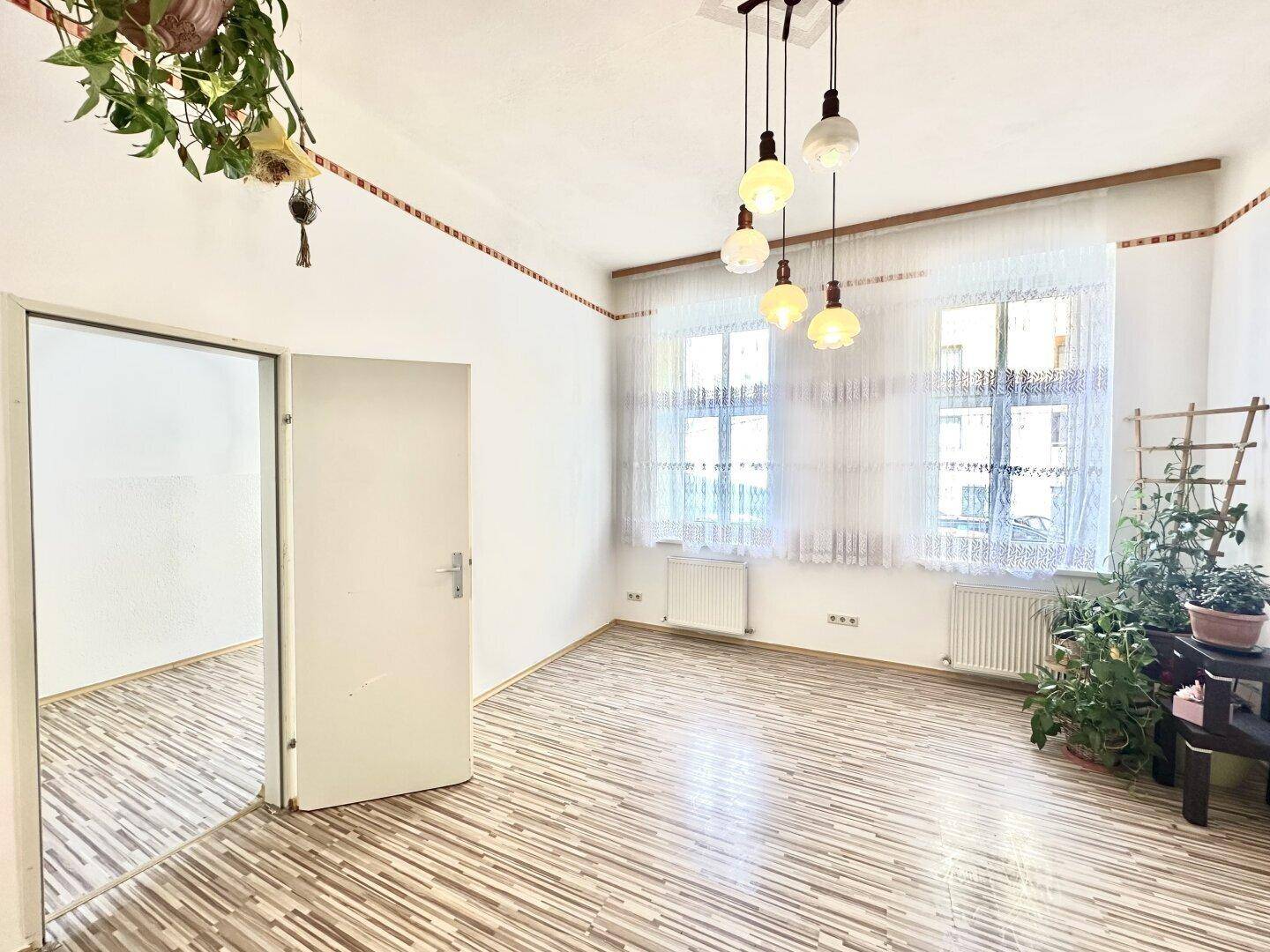 Geräumiger Wohn-Essbereich mit viel Tageslicht, Laminatboden und Zugang zu einem weiteren Raum.