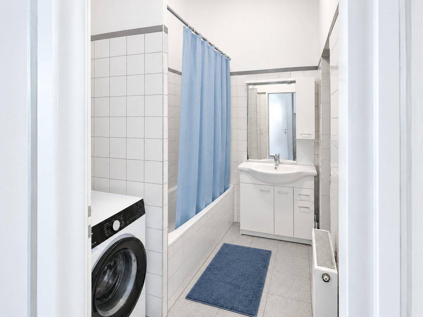 Badezimmer mit Badewanne, Waschmaschine, Waschbecken und weißen Fliesen an den Wänden.