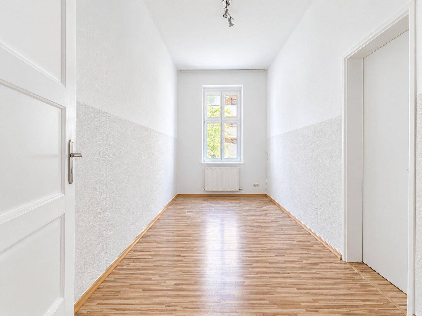 Langer, schmaler Raum mit Laminatboden und einem Fenster, das Tageslicht hereinlässt.