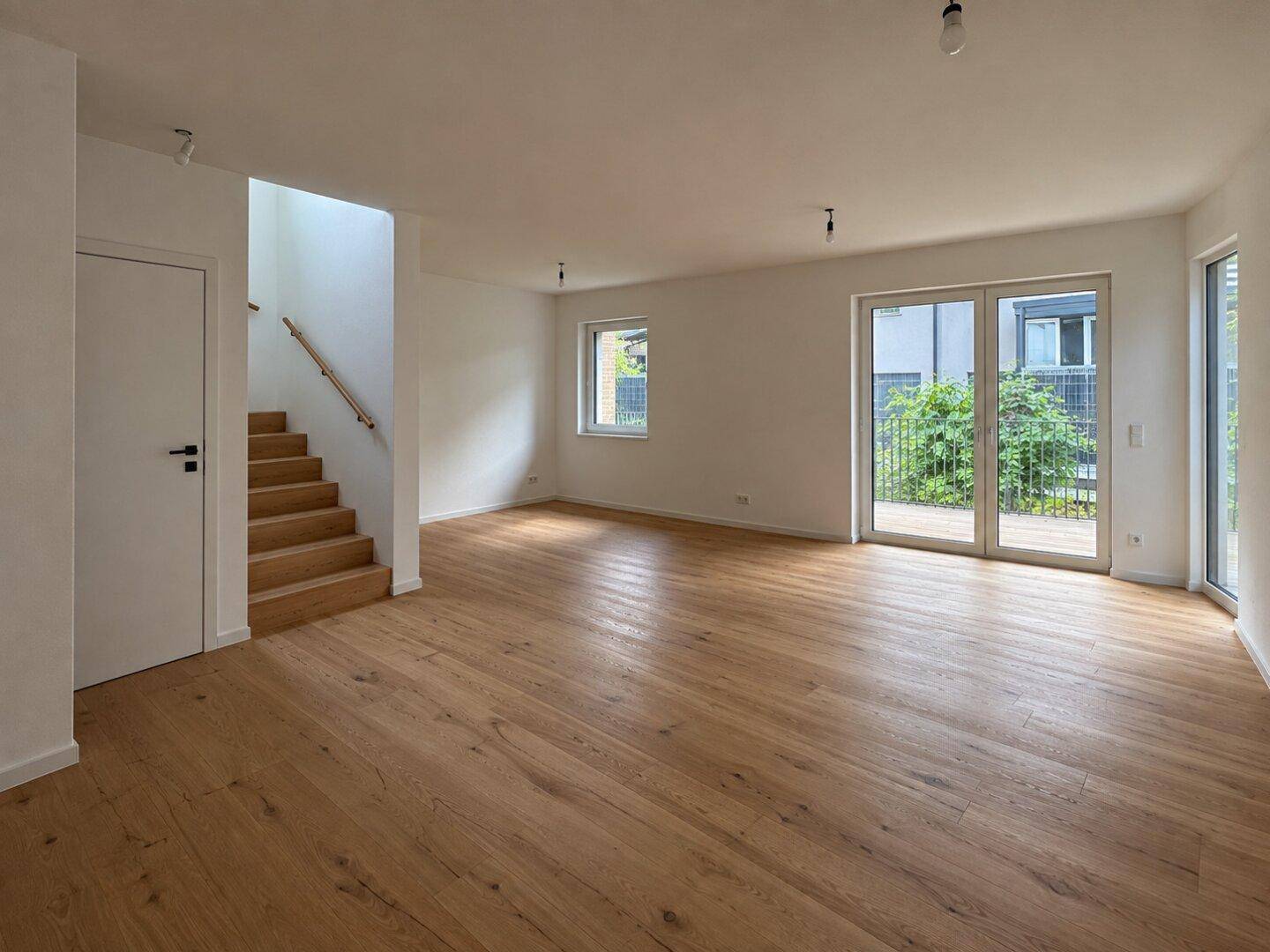 Heller, leerer Wohnbereich mit Eichenparkett, weißen Wänden und Zugang zur Terrasse.