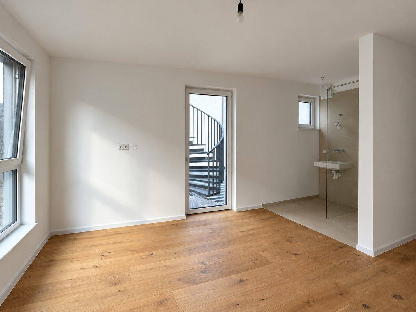 Helles Schlafzimmer mit Holzboden, großen Fenstern und integriertem Duschbereich.