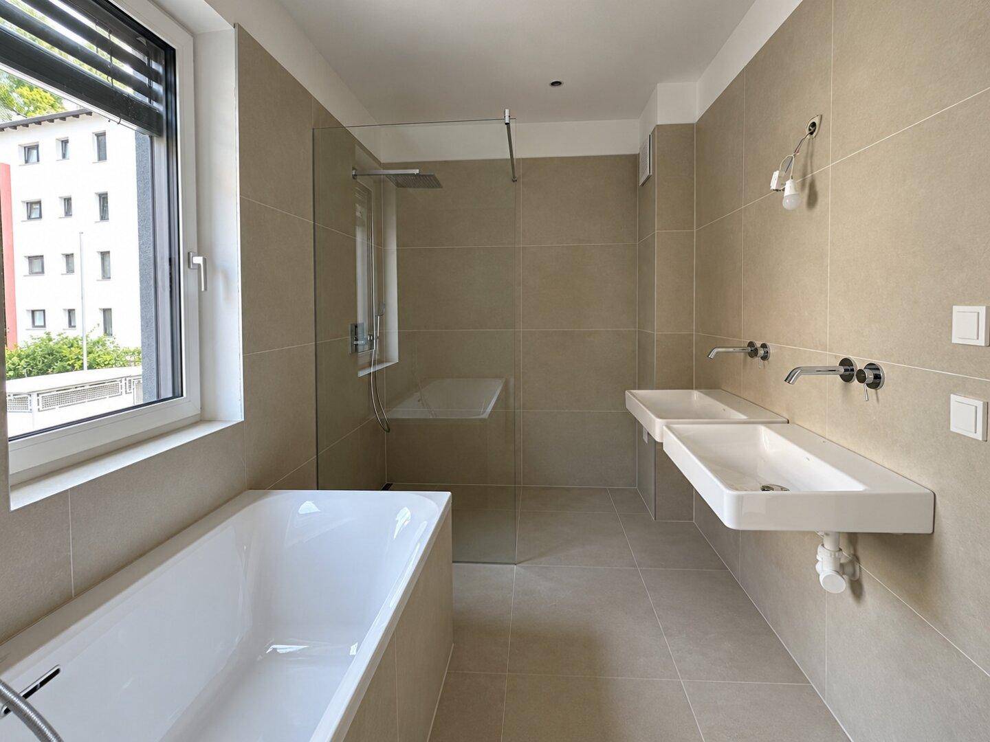 Modernes Badezimmer mit beigefarbenen Fliesen, Badewanne, begehbarer Dusche und Doppelwaschbecken.