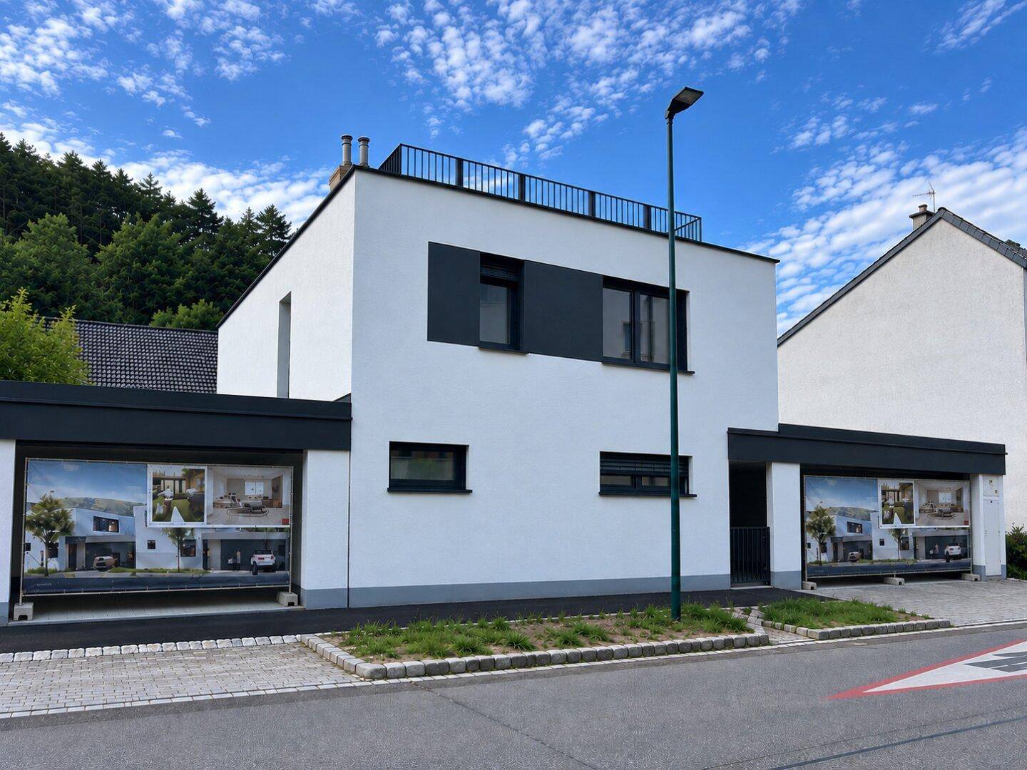 Moderne weiße Fassade eines Neubaus mit Flachdach und integrierten Garagen.