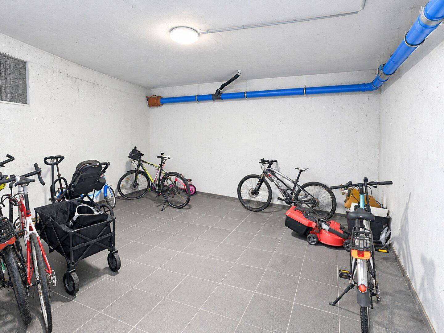 Gemeinschaftlicher Fahrradraum im Untergeschoss mit Fliesenboden und sichtbaren Versorgungsleitungen.