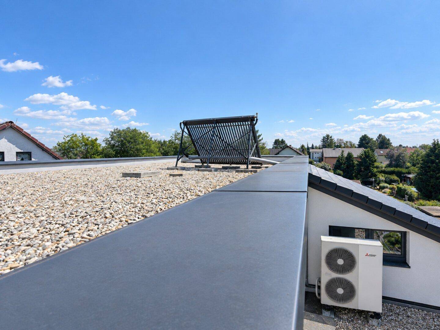 Flachdach mit Solaranlage und Wärmepumpe unter blauem Himmel.
