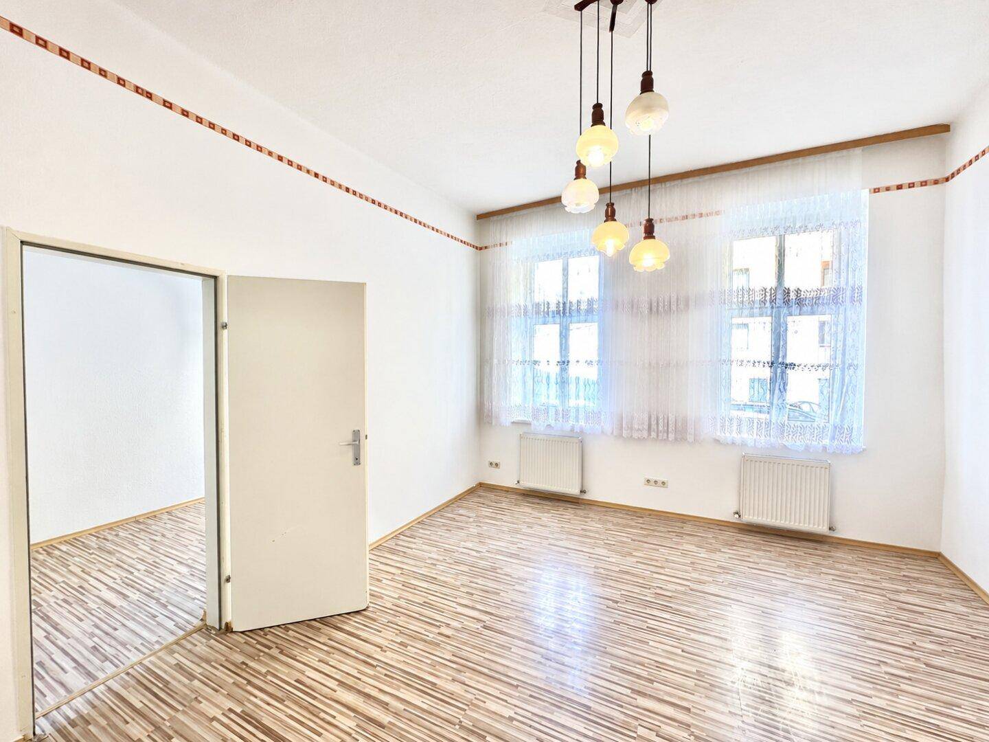 Geräumiges Zimmer mit Holzfußboden und viel Tageslicht, offen zu einem weiteren Raum.