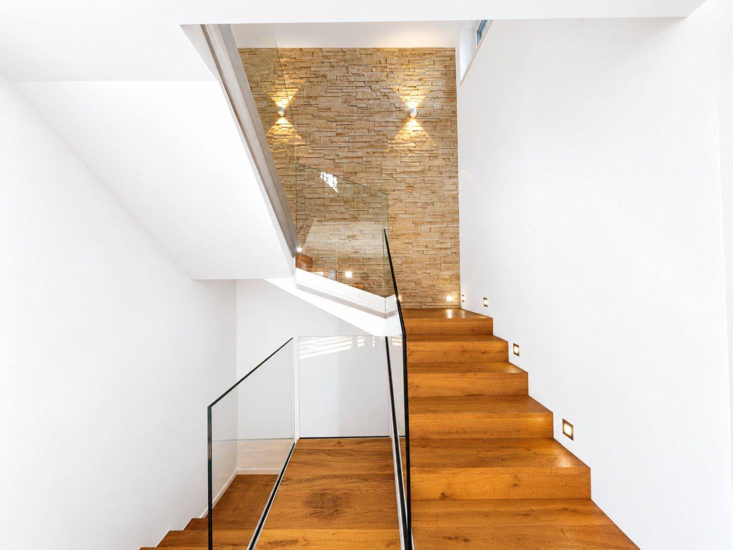 Elegante Holztreppe mit Glasgeländer und dekorativer Steinwandbeleuchtung.