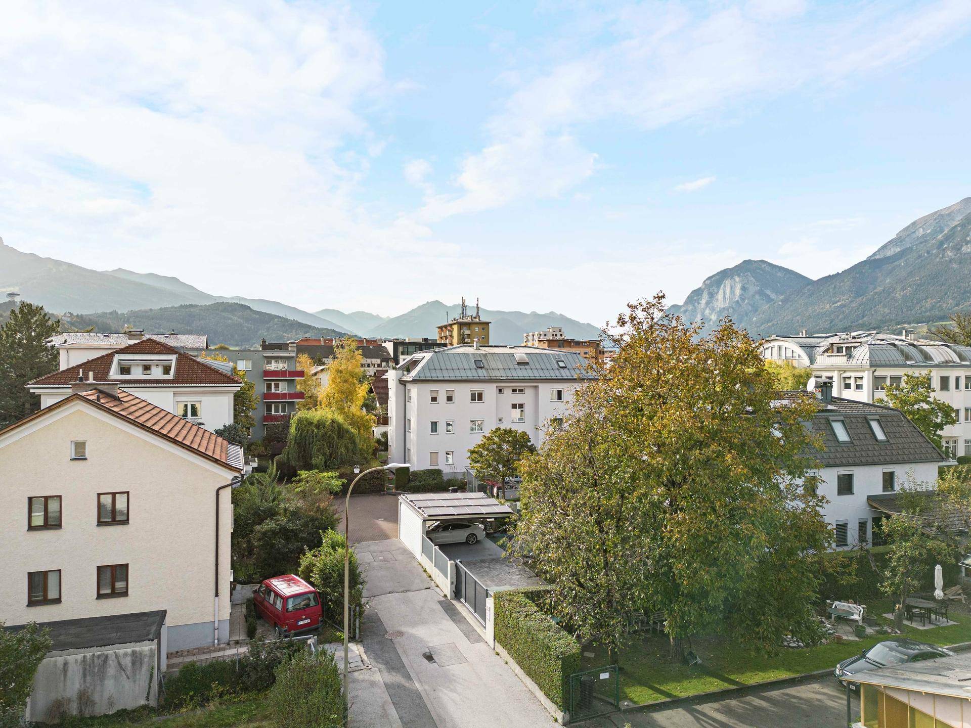 Blick auf eine Wohnstraße mit verschiedenen Gebäuden, Bäumen und einer beeindruckenden Bergkulisse.