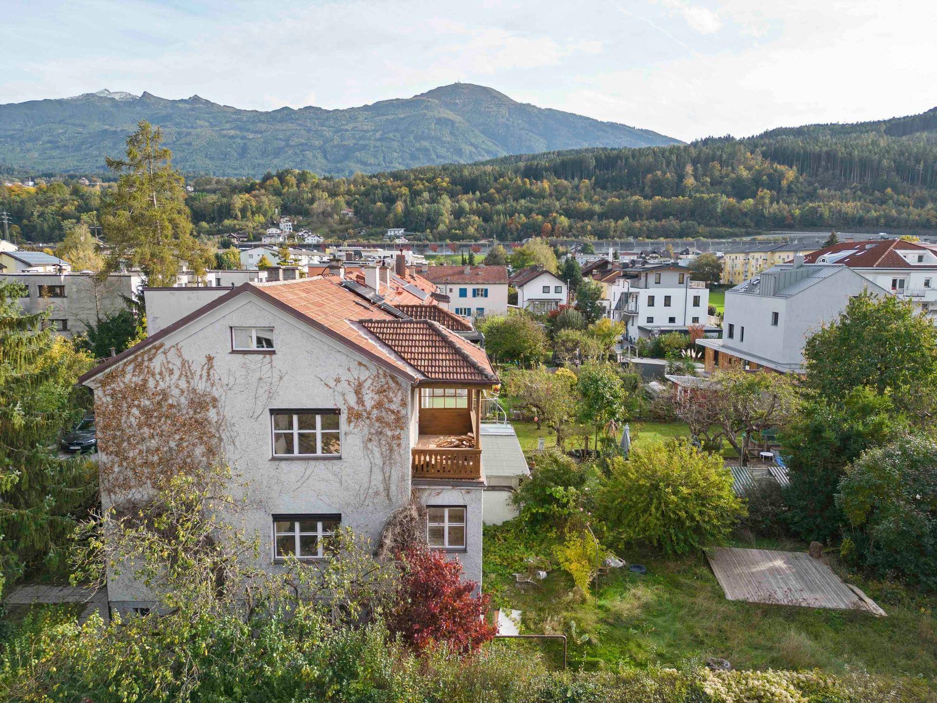 Rückansicht eines Hauses mit kleinem Holzbalkon, üppigem Garten und weitem Blick auf die Berge.