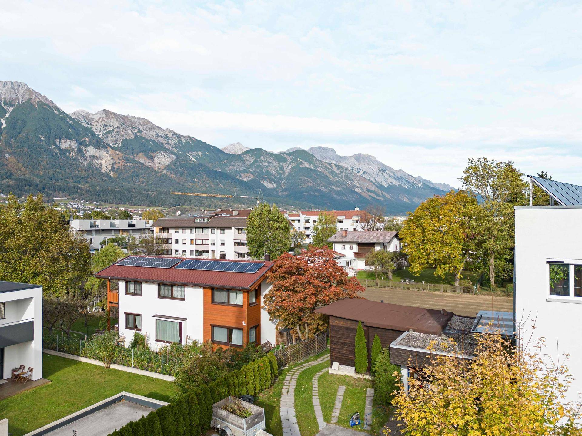 Luftaufnahme einer Wohngegend mit Häusern, grünen Bäumen und beeindruckender Bergkulisse.