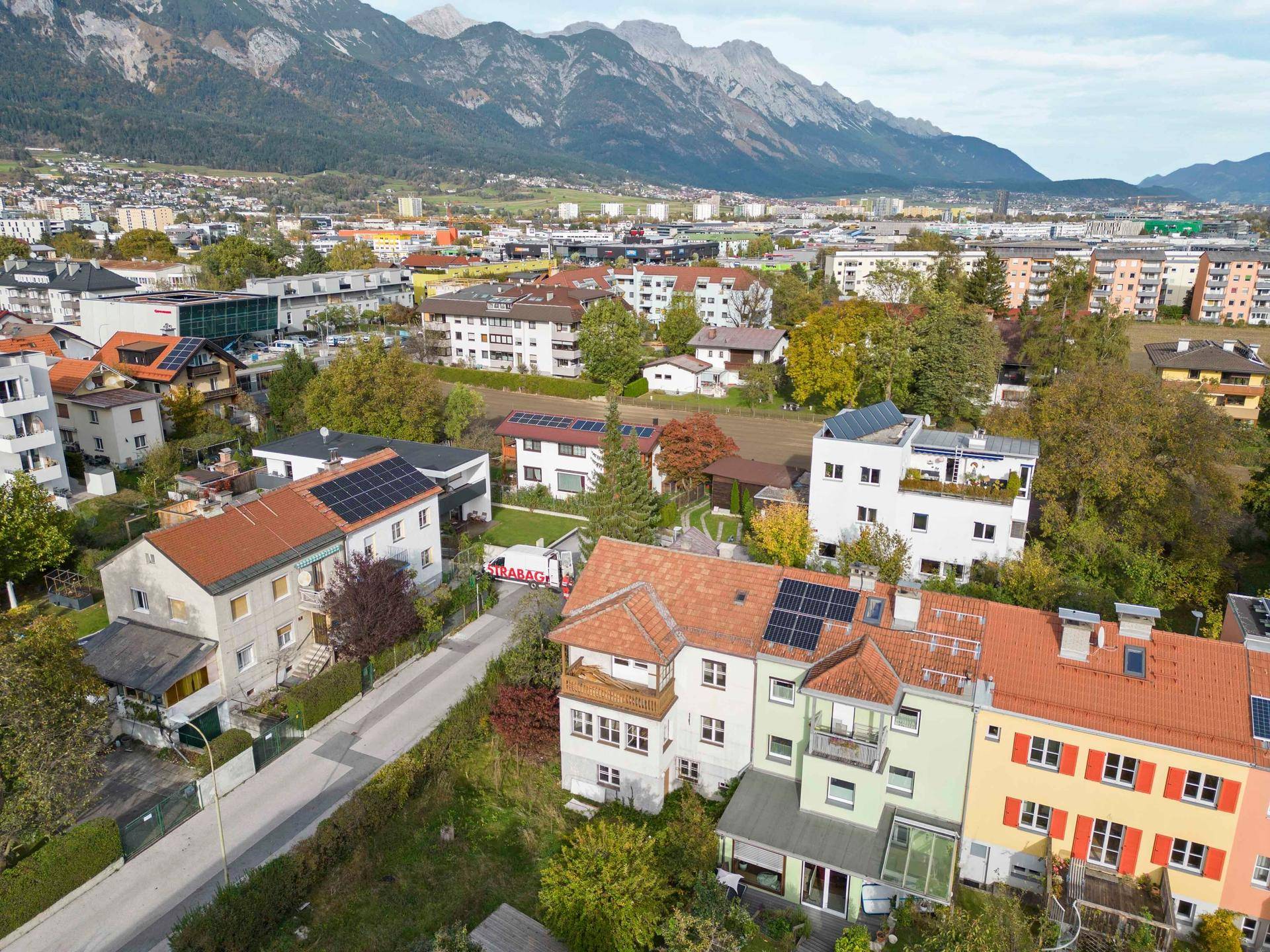 Weitläufige Luftaufnahme einer Wohngegend mit vielfältigen Häusern, Gärten und Solaranlagen unter Bergblick.