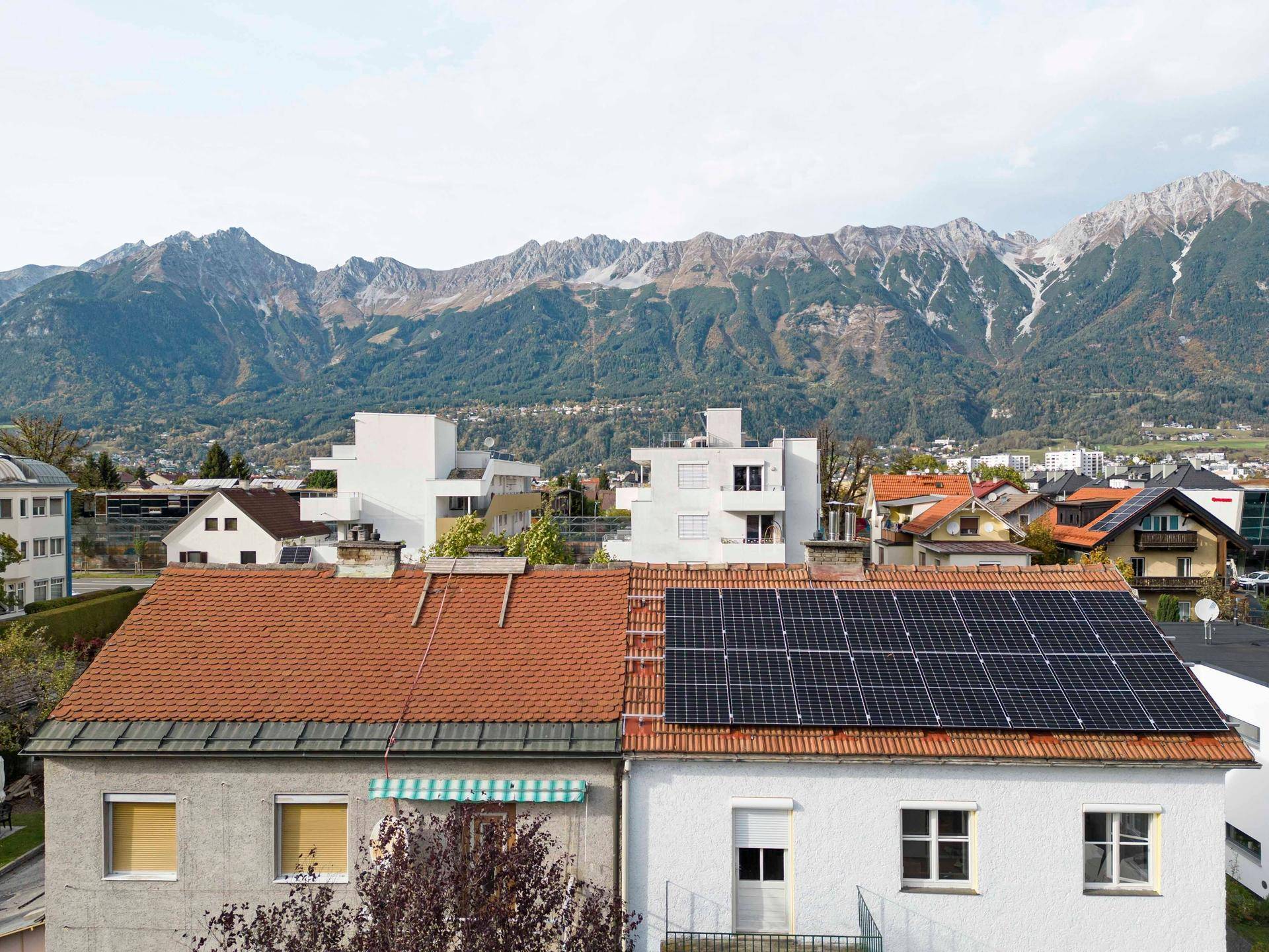 Nahaufnahme von zwei Wohnhäusern mit Solaranlagen auf den Dächern und majestätischem Bergpanorama.