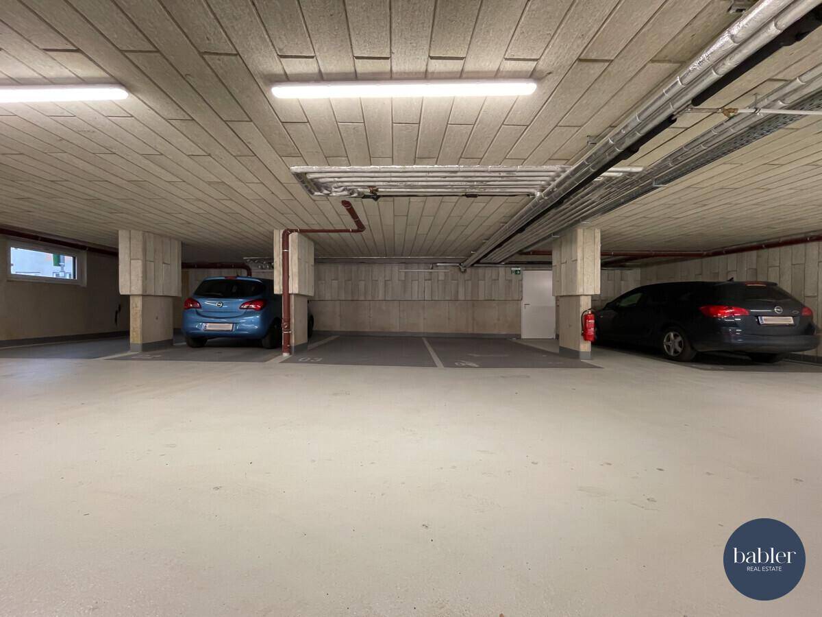 Geräumige Tiefgarage mit Betonpfeilern, sichtbaren Leitungen und ausreichend Parkplätzen.