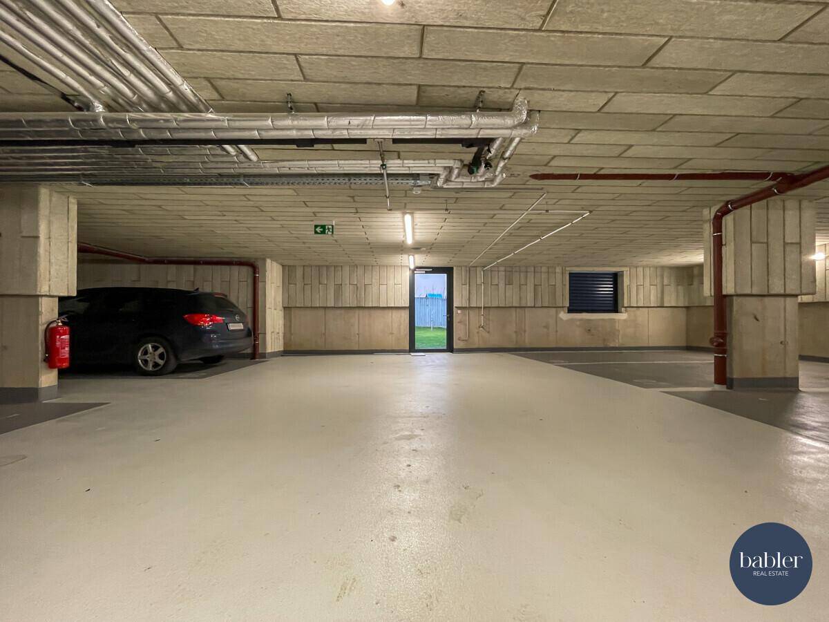 Tiefgarage mit Betonwänden, sichtbaren Installationen und einem Ausgang ins Freie.