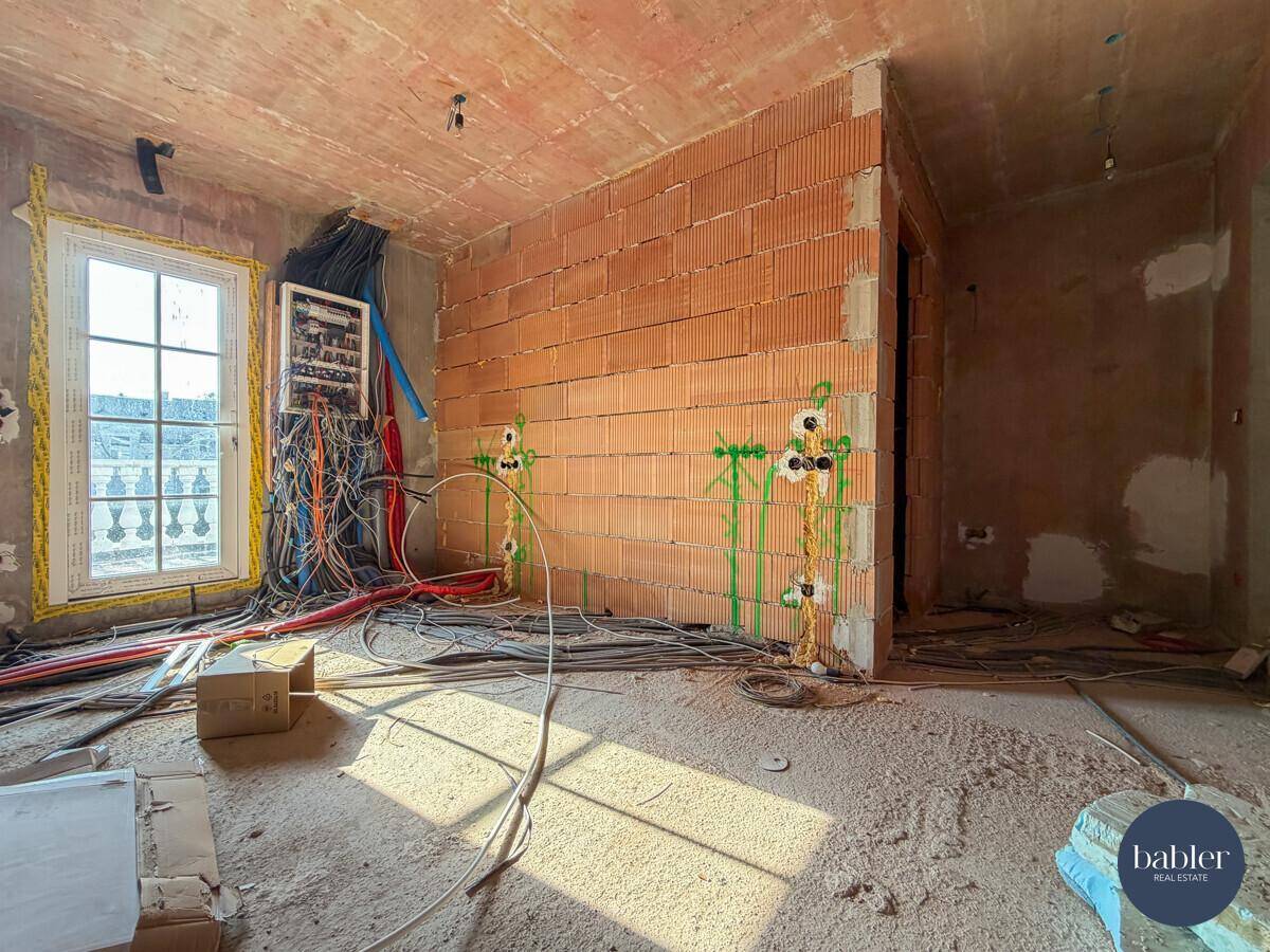 Rohbauzimmer mit unverputzten Wänden, sichtbaren Leitungen und Fenster mit Balkon.