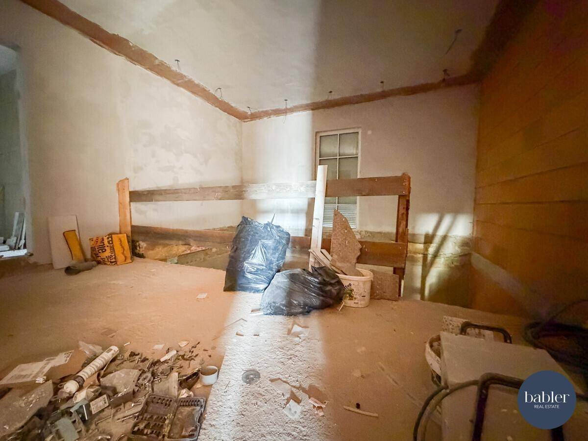 Rohbauzimmer mit Bauabfällen, Fenster und vorbereiteten Wänden für den Innenausbau.