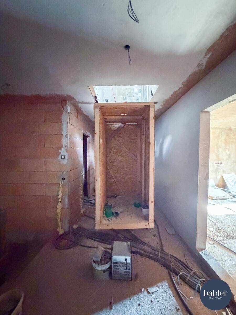 Rohbauflur mit vorbereitetem Aufzugschacht und sichtbaren Installationen.