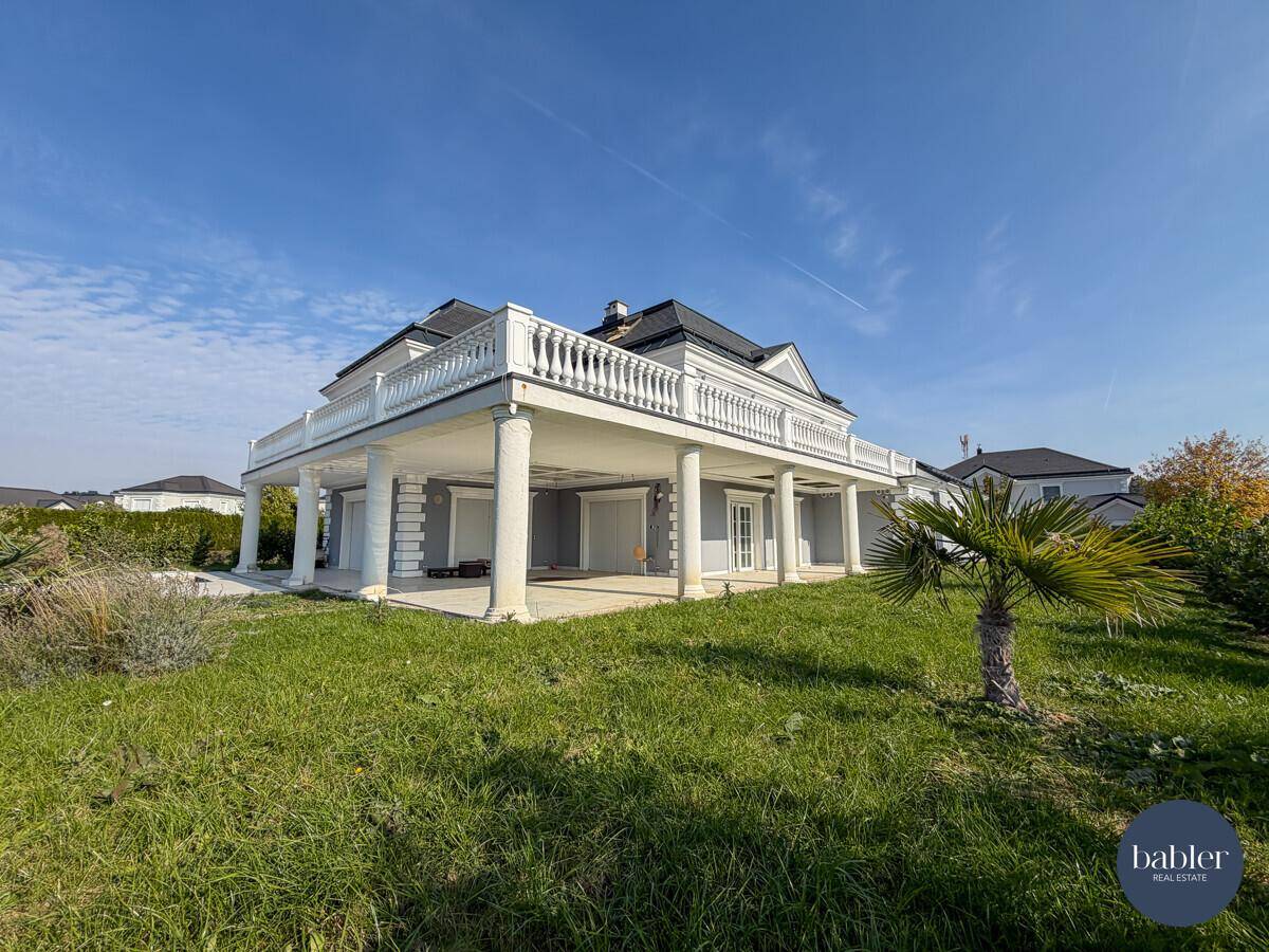 Rückansicht der Villa mit großer überdachter Terrasse und weitläufigem Garten.