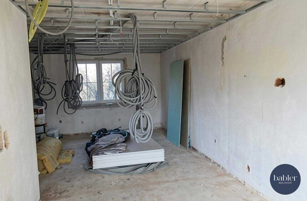 Raum im Rohbau mit sichtbaren Leitungen und Baumaterialien, bereit für den Ausbau.