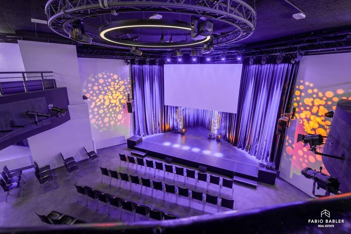 Großer Veranstaltungssaal mit Bühne, Bestuhlung und professioneller Beleuchtungstechnik für Events.