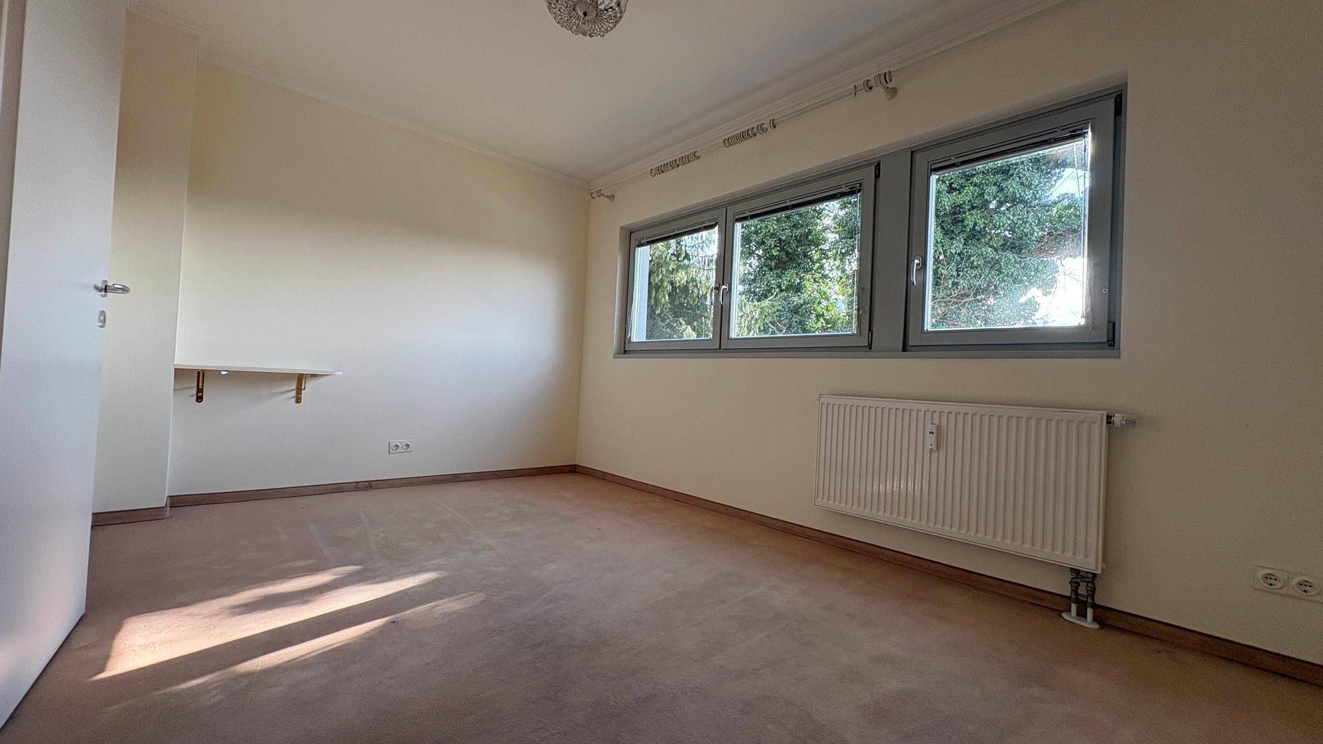 Geräumiges Schlafzimmer mit Teppichboden und drei Fenstern, die viel Tageslicht hereinlassen.