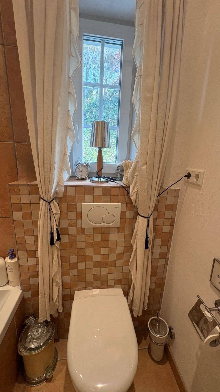 Badezimmer mit WC, Fenster und Fliesen in warmen Farbtönen.