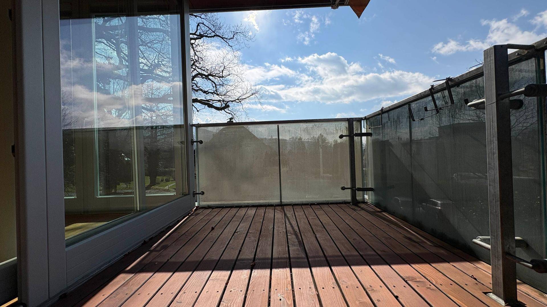 Geräumiger Balkon mit Holzboden und Glasgeländer, bietet einen sonnigen Platz im Freien.