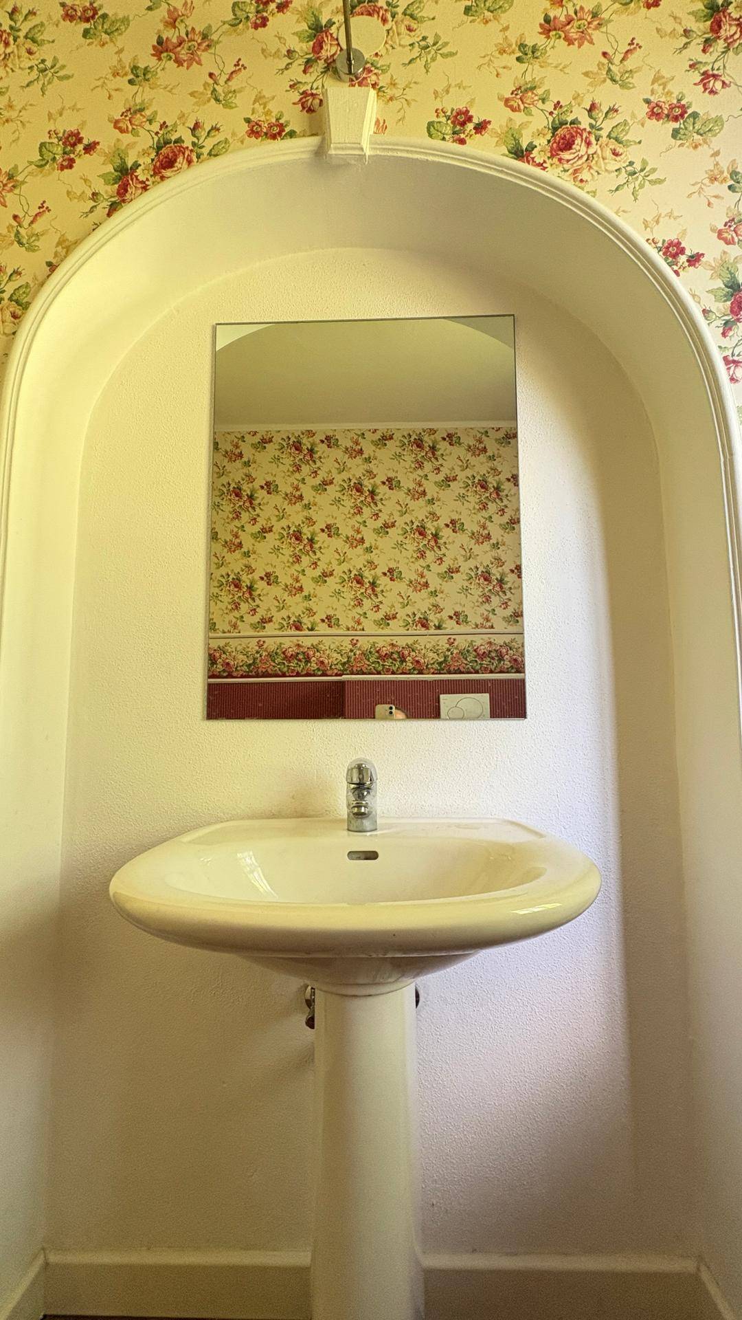 Waschbecken in der Gästetoilette mit floraler Tapete und einem Spiegel in einer Nische.