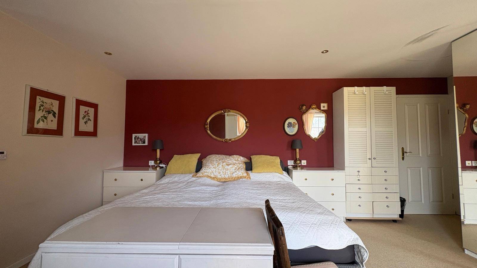 Geräumiges Schlafzimmer mit Doppelbett, roten Wänden und weißen Schränken.