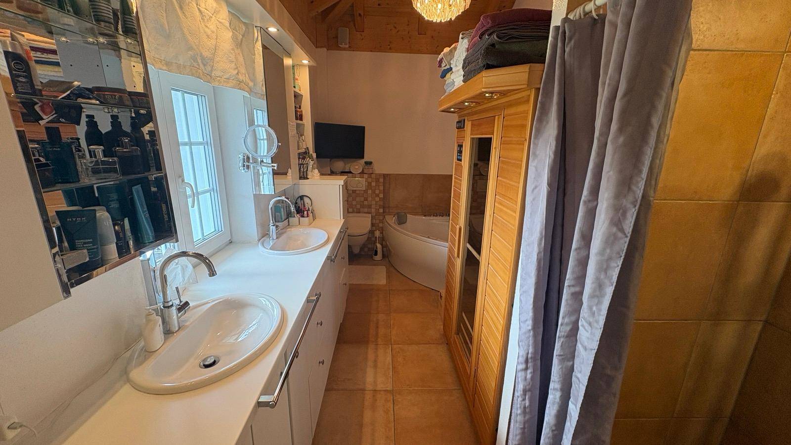 Badezimmer mit Doppelwaschbecken, Sauna und Badewanne im Hintergrund.