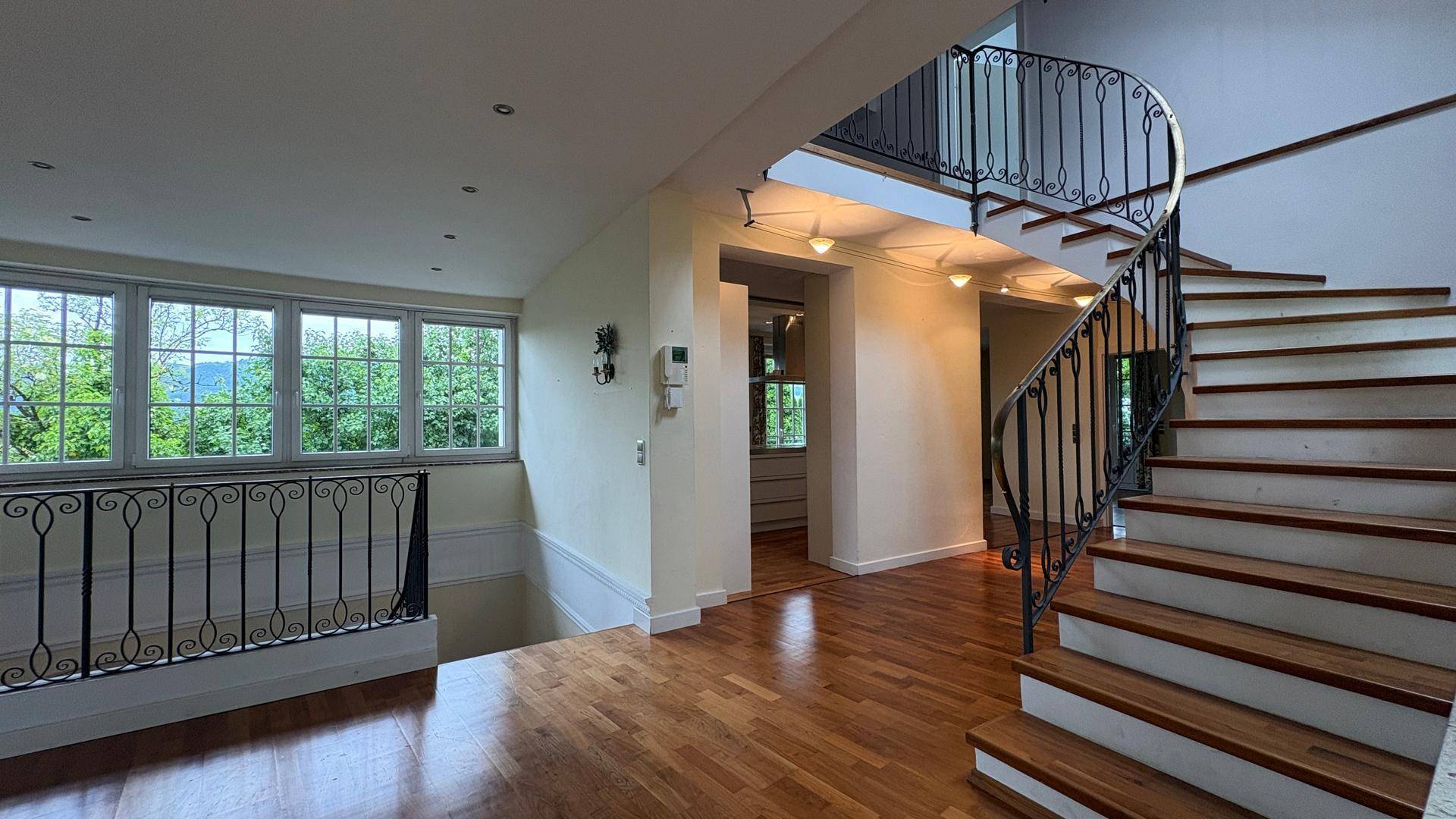 Elegante Holztreppe mit schmiedeeisernem Geländer und Blick auf den hellen Wohnbereich.