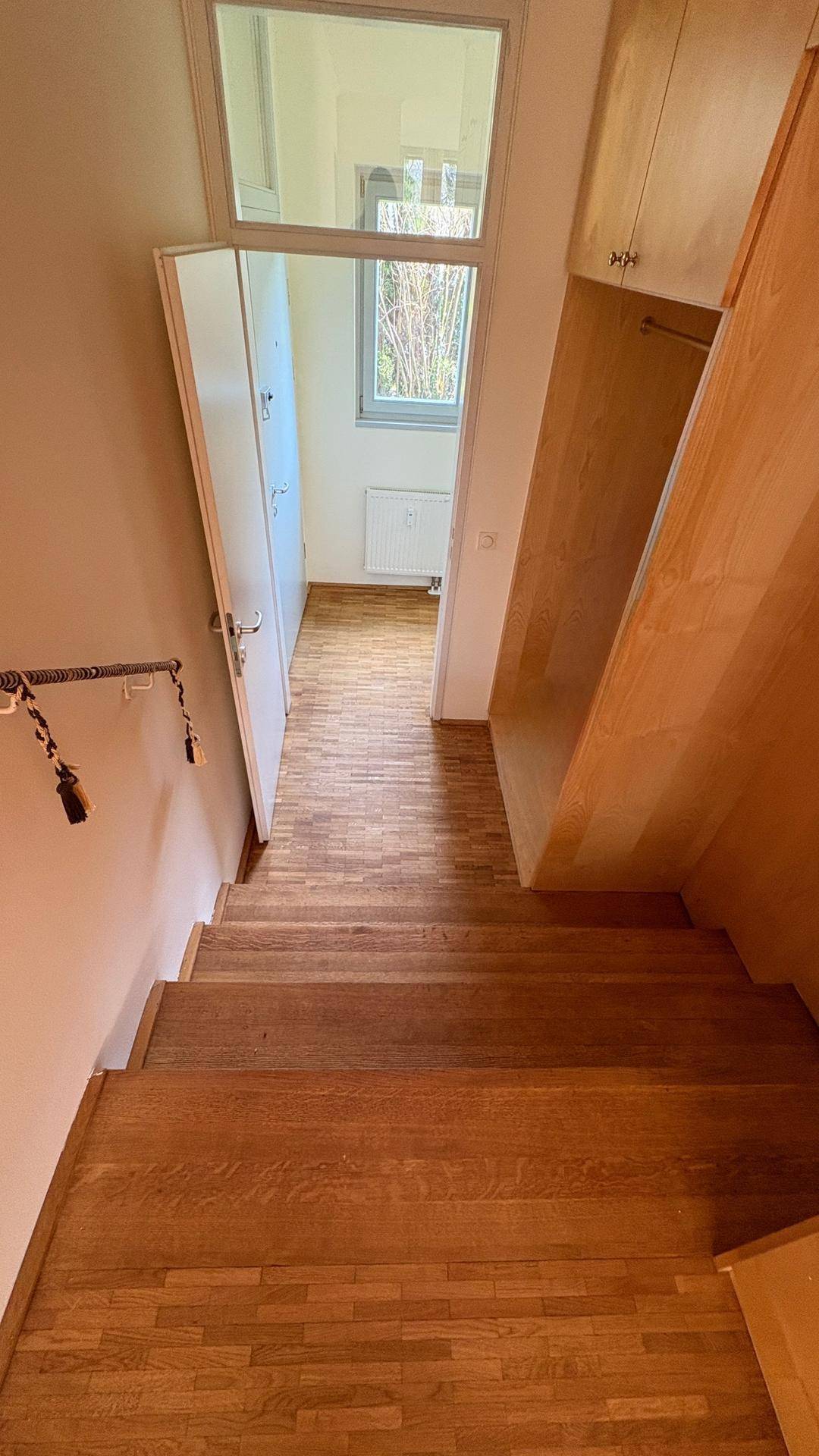 Treppenaufgang mit Holzstufen und Parkettboden, der zu einem hellen Bereich mit Fenster führt.
