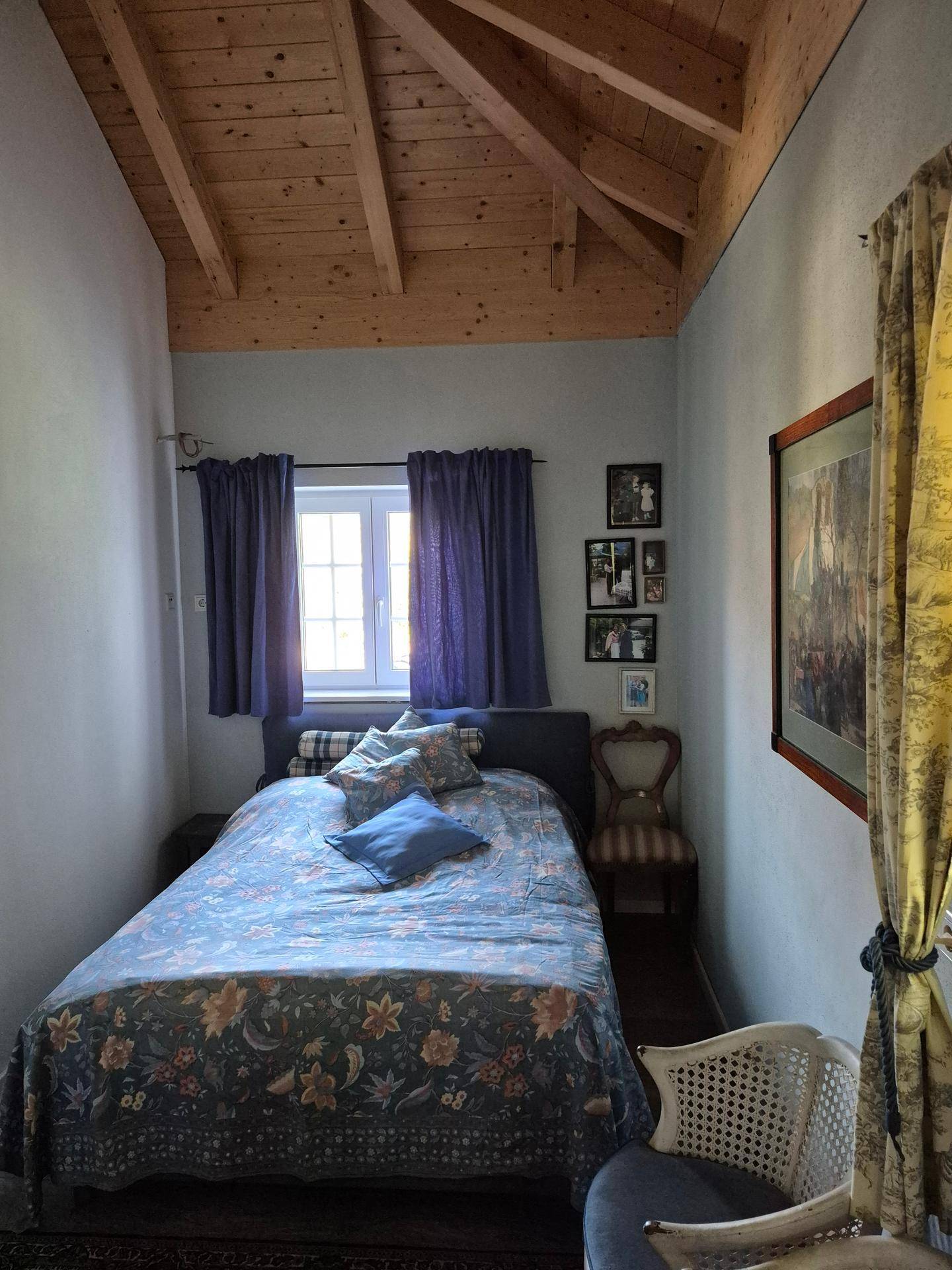 Schlafzimmer mit Holzbalkendecke, Einzelbett und Fenster mit Vorhängen.