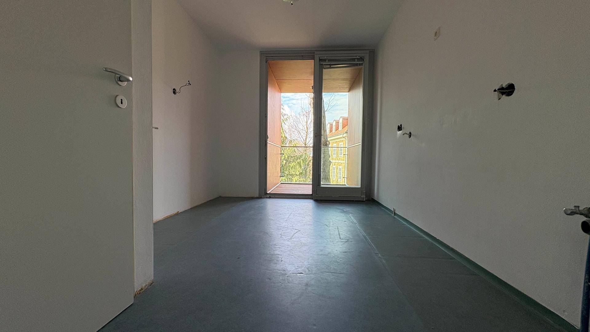 Leerer Raum mit Balkonzugang und vorbereiteten Anschlüssen, ideal für eine Küche oder ein weiteres Zimmer.