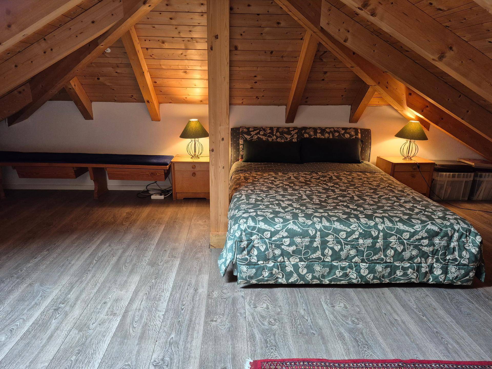 Gemütliches Schlafzimmer im Dachgeschoss mit Holzbalken und Laminatboden.