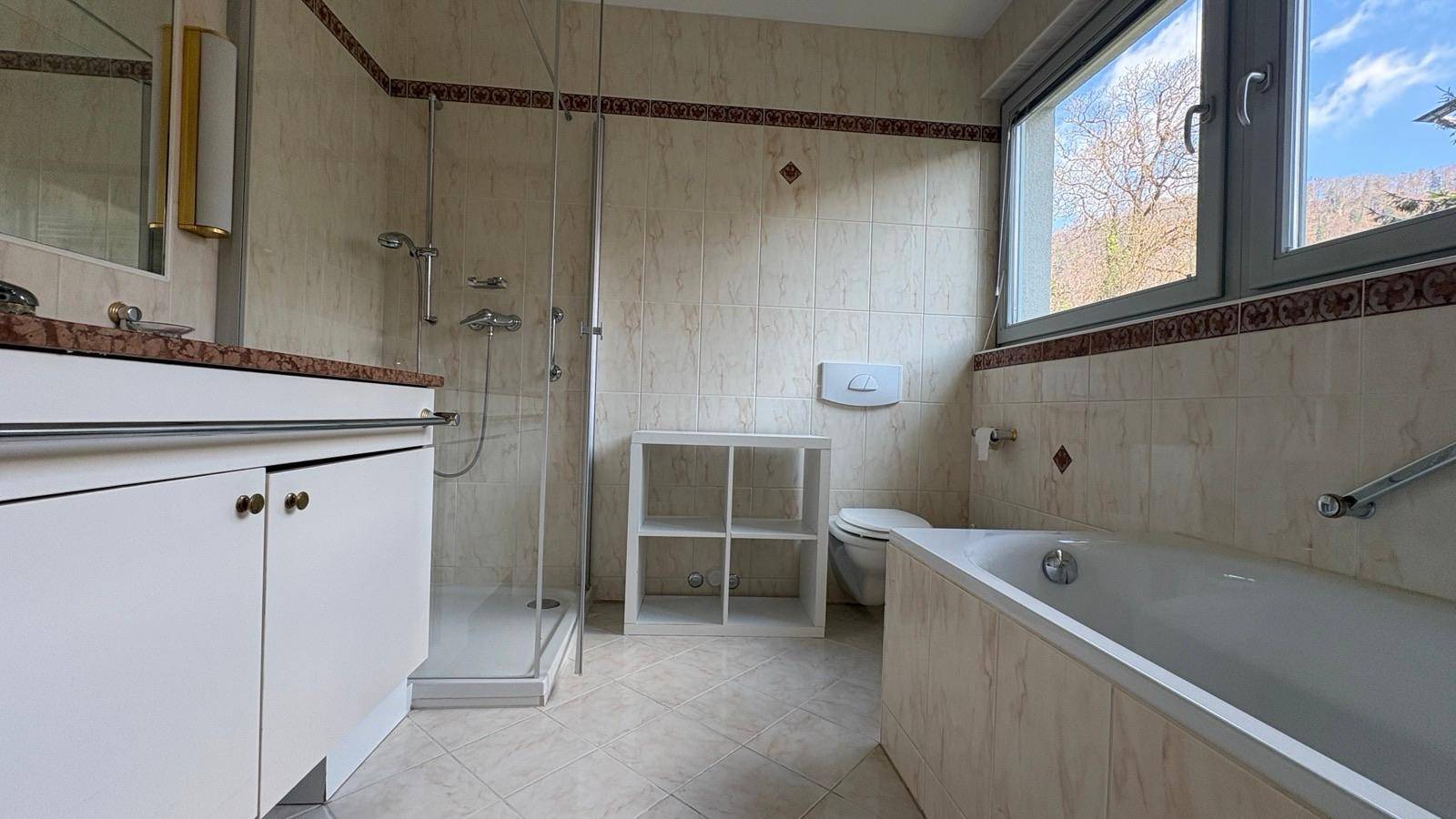 Badezimmer mit Badewanne, Dusche, WC und Fenster, ausgestattet mit hellen Fliesen.