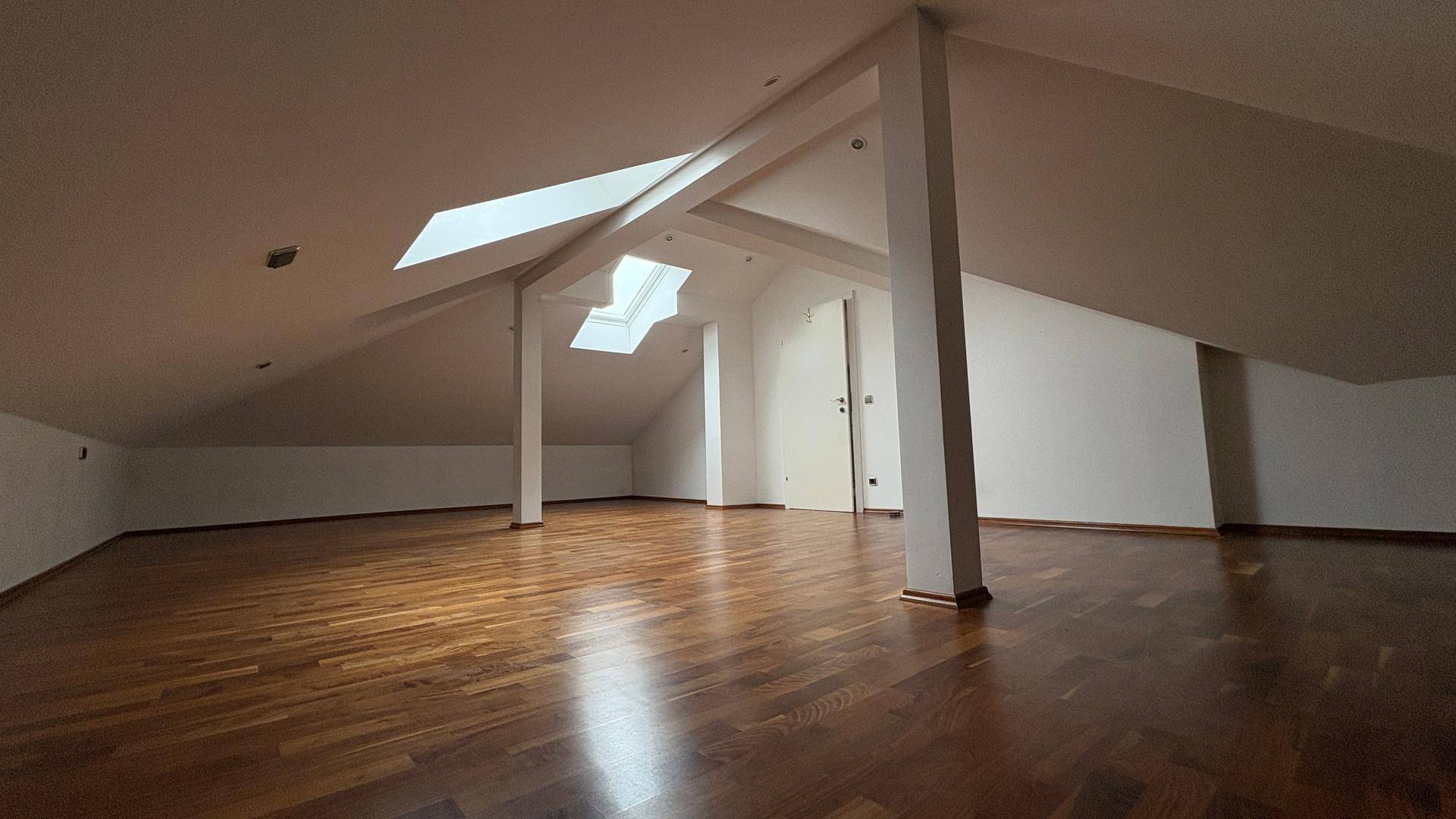 Geräumiger Dachbodenraum mit Holzboden, Dachschrägen und mehreren Dachfenstern.