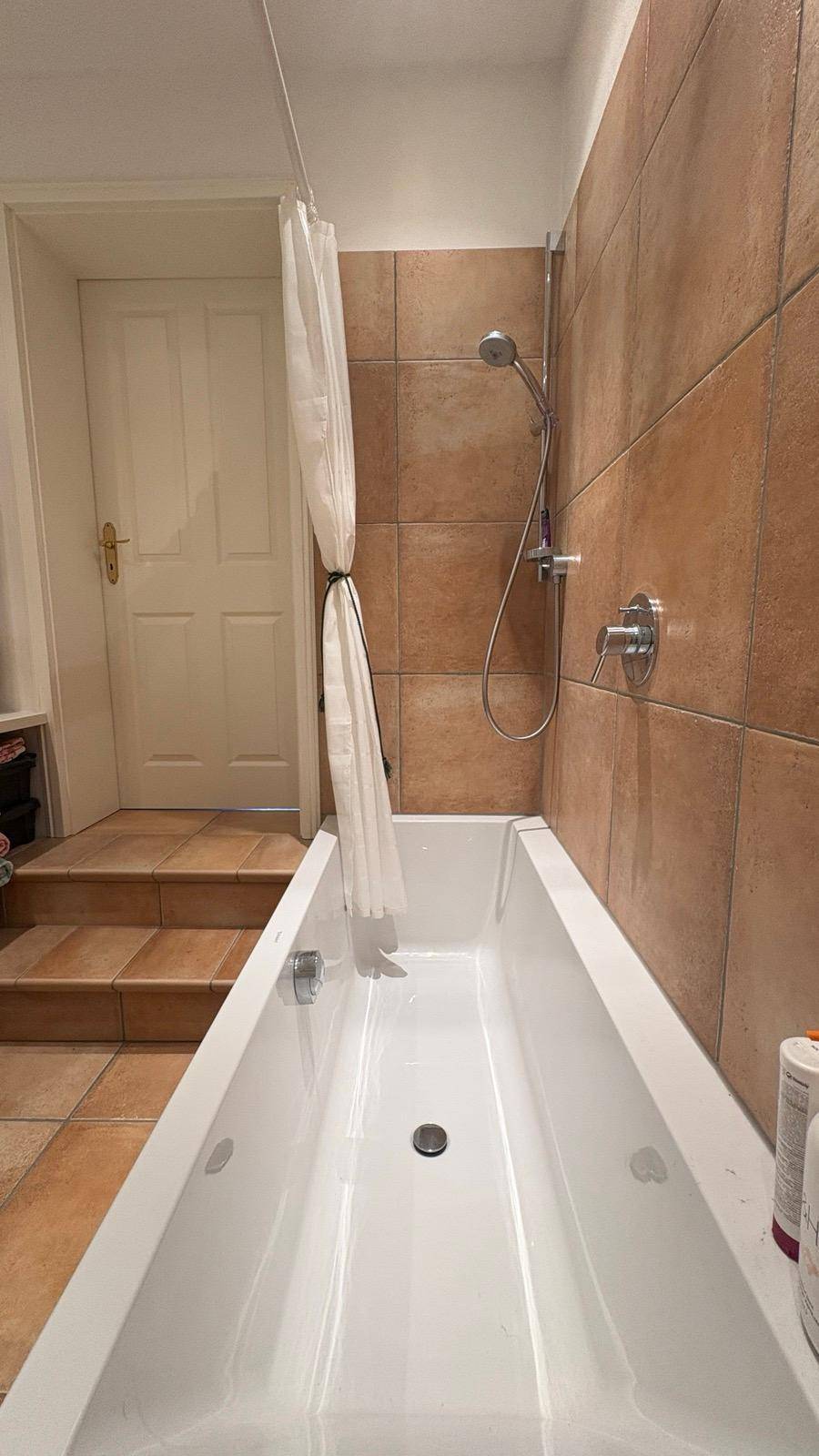 Badezimmer mit Badewanne und braunen Fliesen an den Wänden.