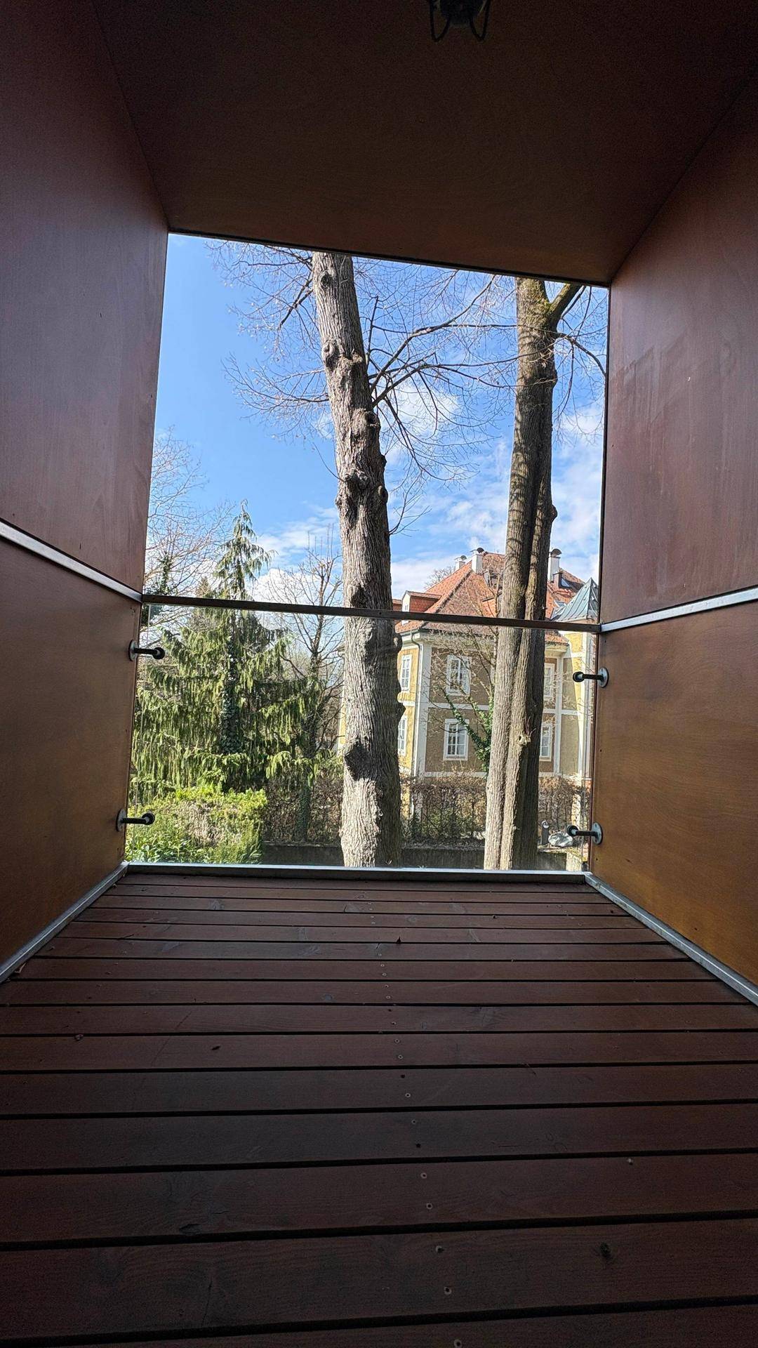 Überdachte Loggia mit Holzboden und Blick auf alte Bäume und die umliegende Bebauung.