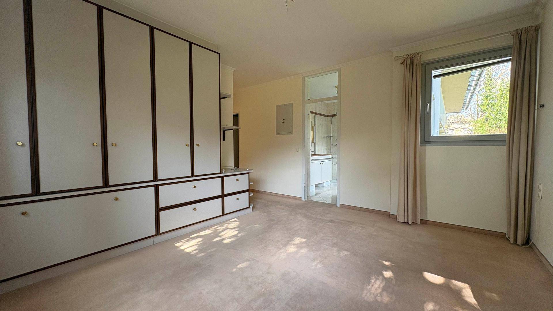 Helles Schlafzimmer mit Teppichboden und direktem Zugang zu einem angrenzenden Badezimmer.