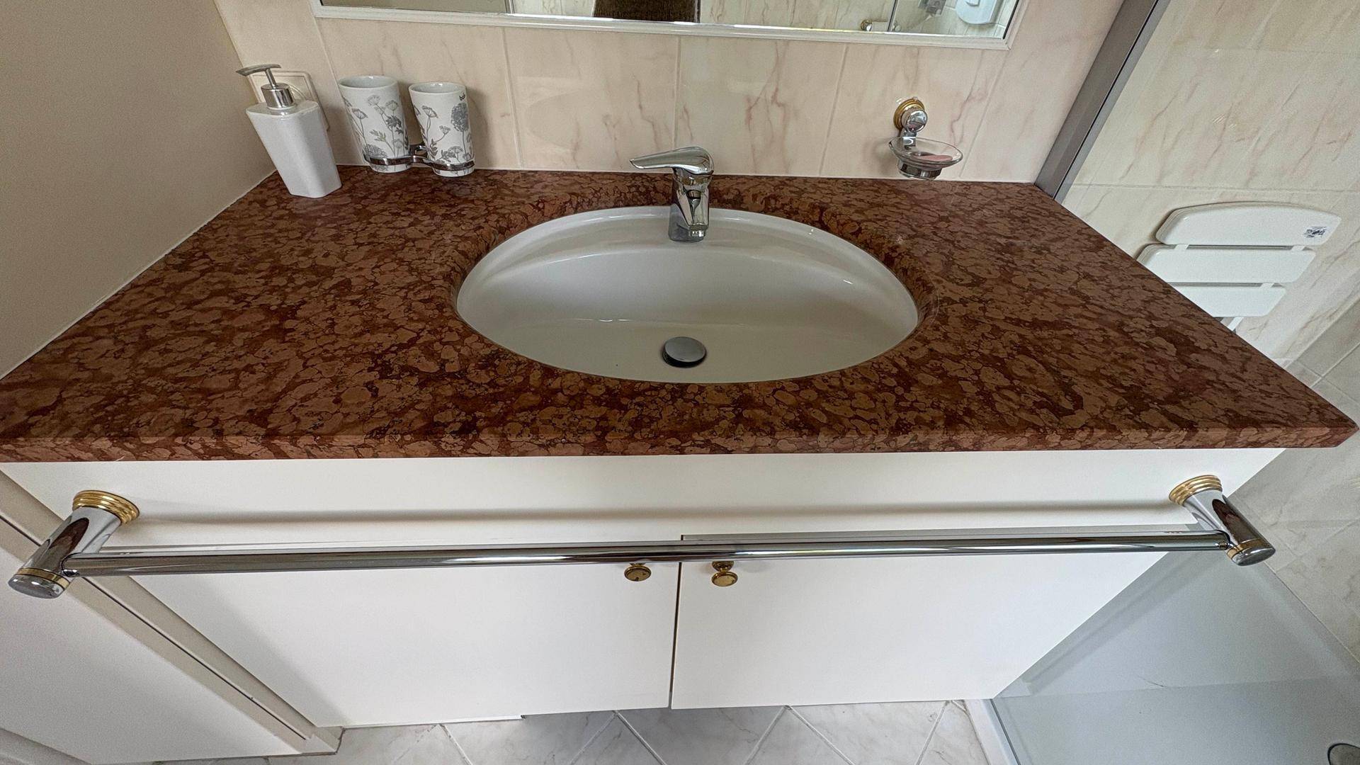Waschbecken mit brauner Marmor-Arbeitsplatte und weißen Unterschränken im Badezimmer.