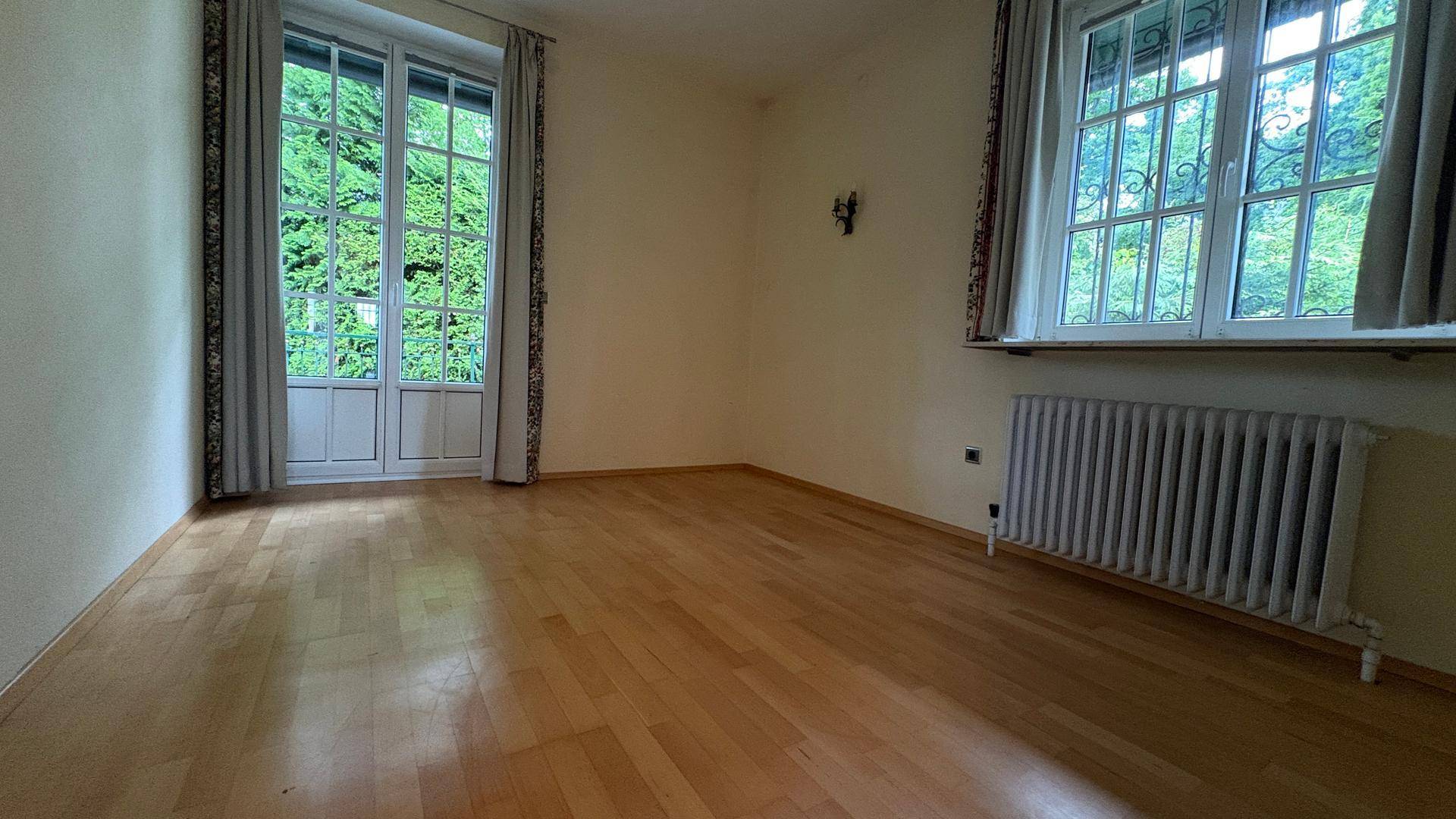Helles Zimmer mit Holzboden, großem Fenster und Zugang zu einem französischen Balkon.
