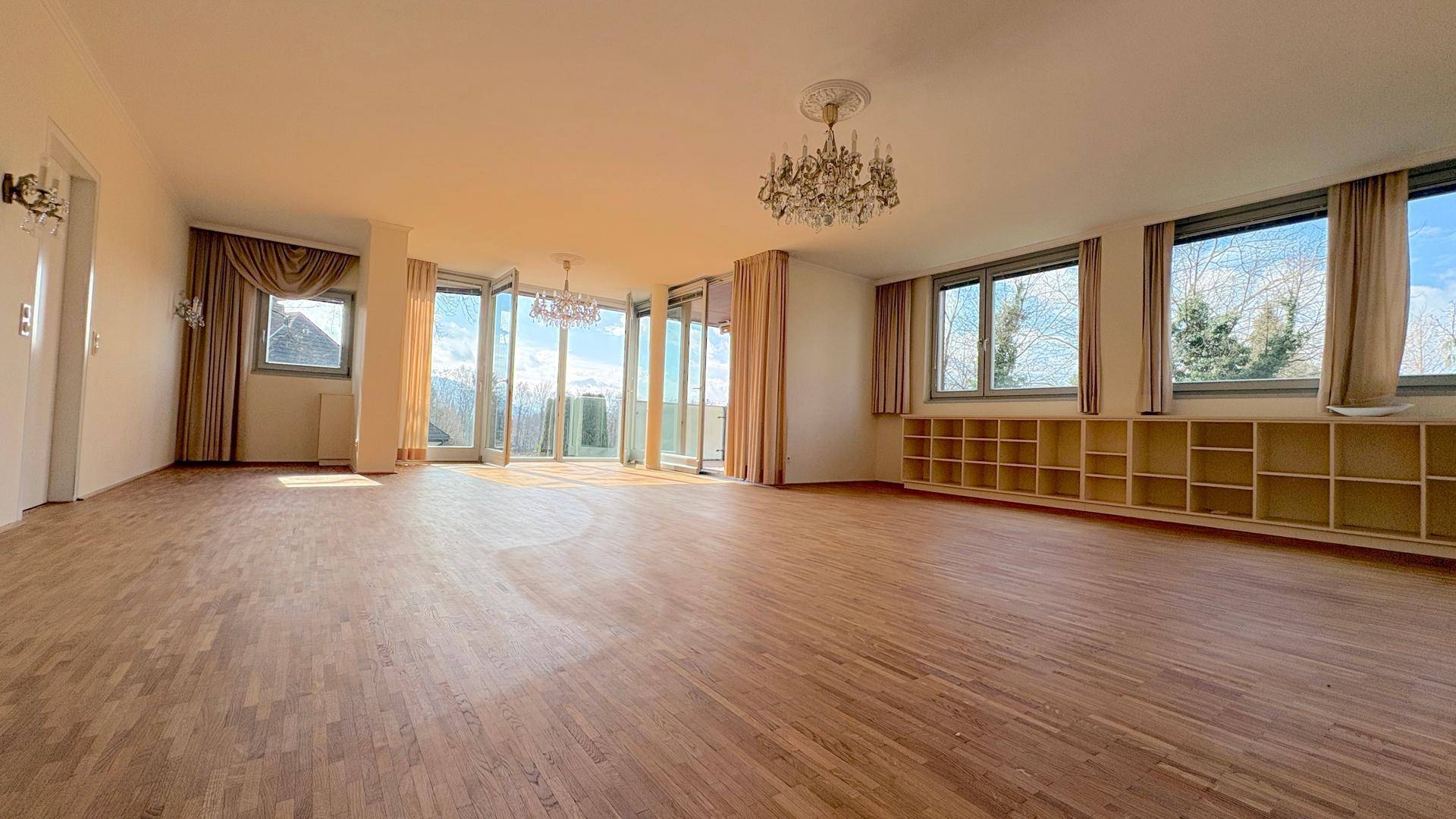 Großzügiges, lichtdurchflutetes Wohnzimmer mit Parkettboden, Kronleuchtern und Zugang zum Balkon.