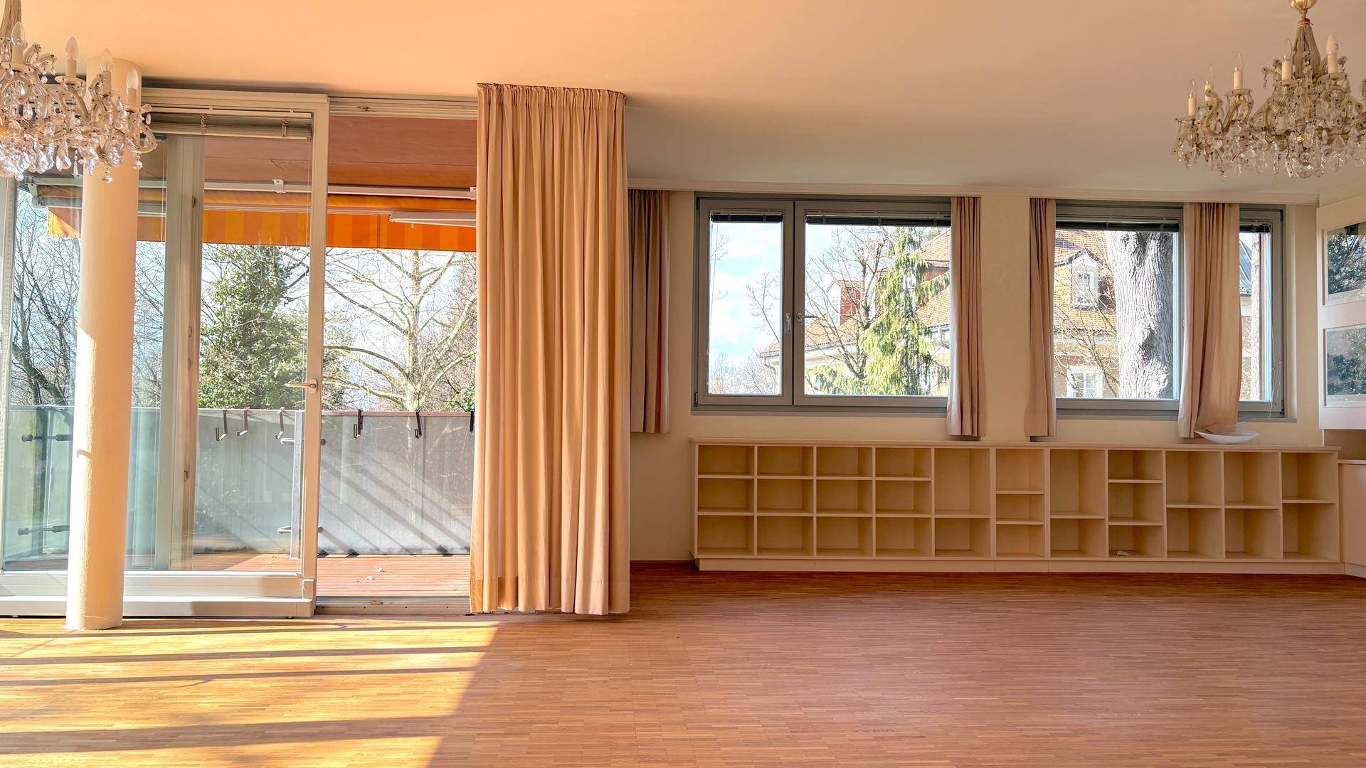 Geräumiges Wohnzimmer mit Parkettboden, großen Fenstern und Schiebetür zum Außenbereich.