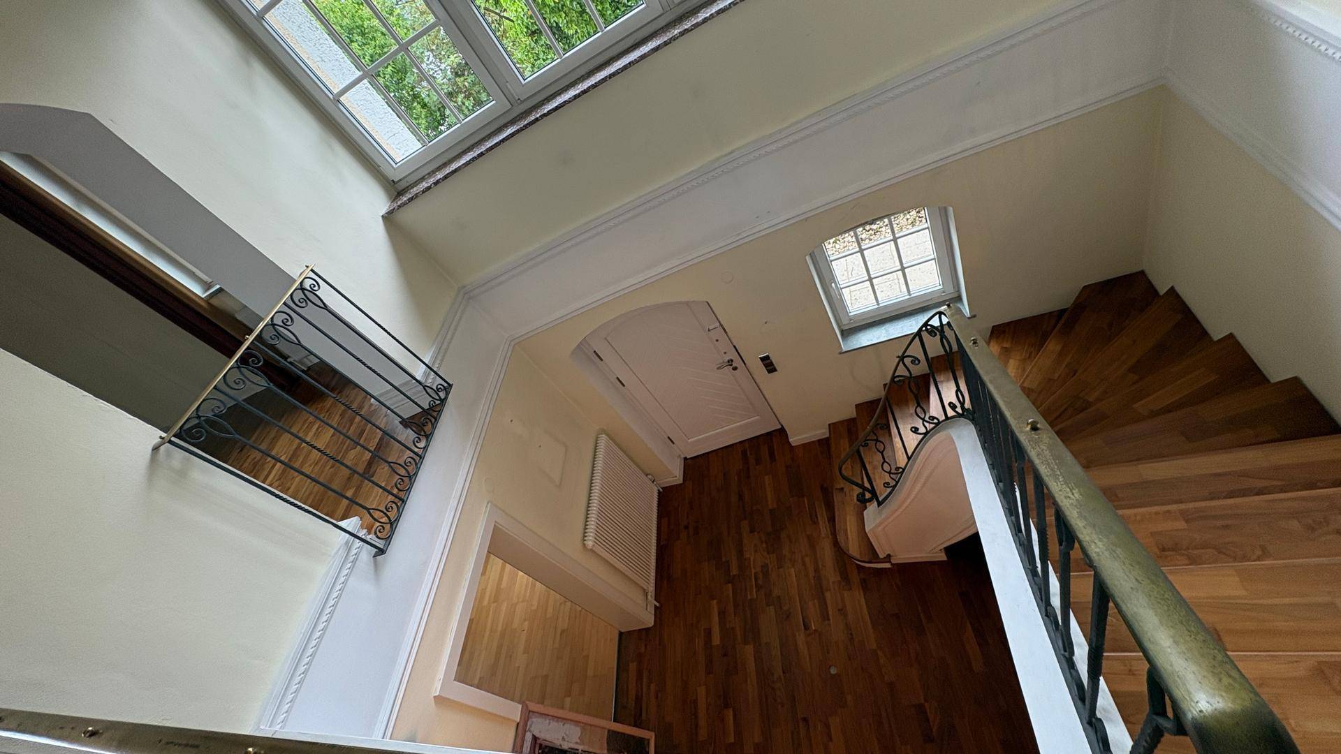 Blick von oben auf eine elegante Holztreppe und den hellen Flur mit hohen Decken.