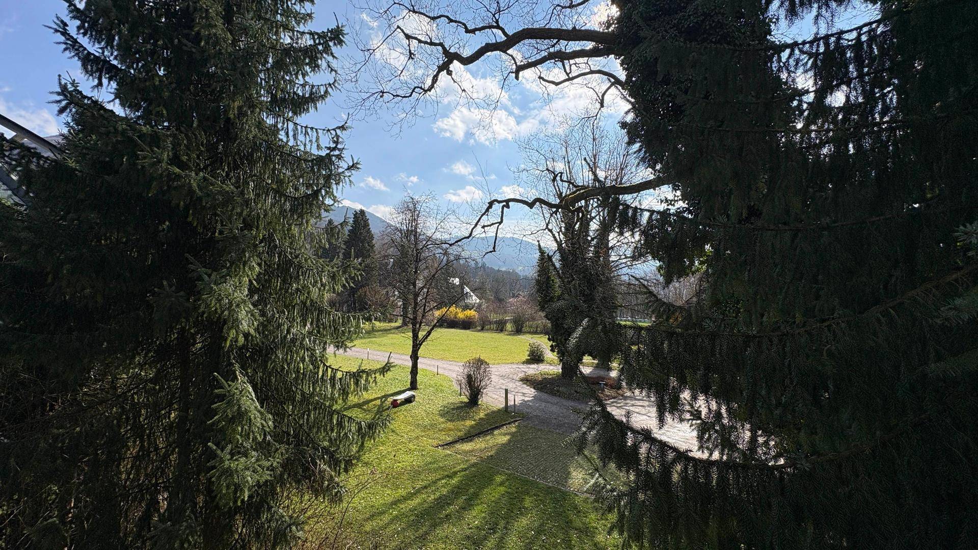 Malerischer Ausblick auf eine weite grüne Landschaft mit Bäumen und Bergen im Hintergrund unter blauem Himmel.