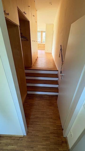 Heller Flur mit Holzparkettboden und Treppe, umgeben von Einbauschränken.