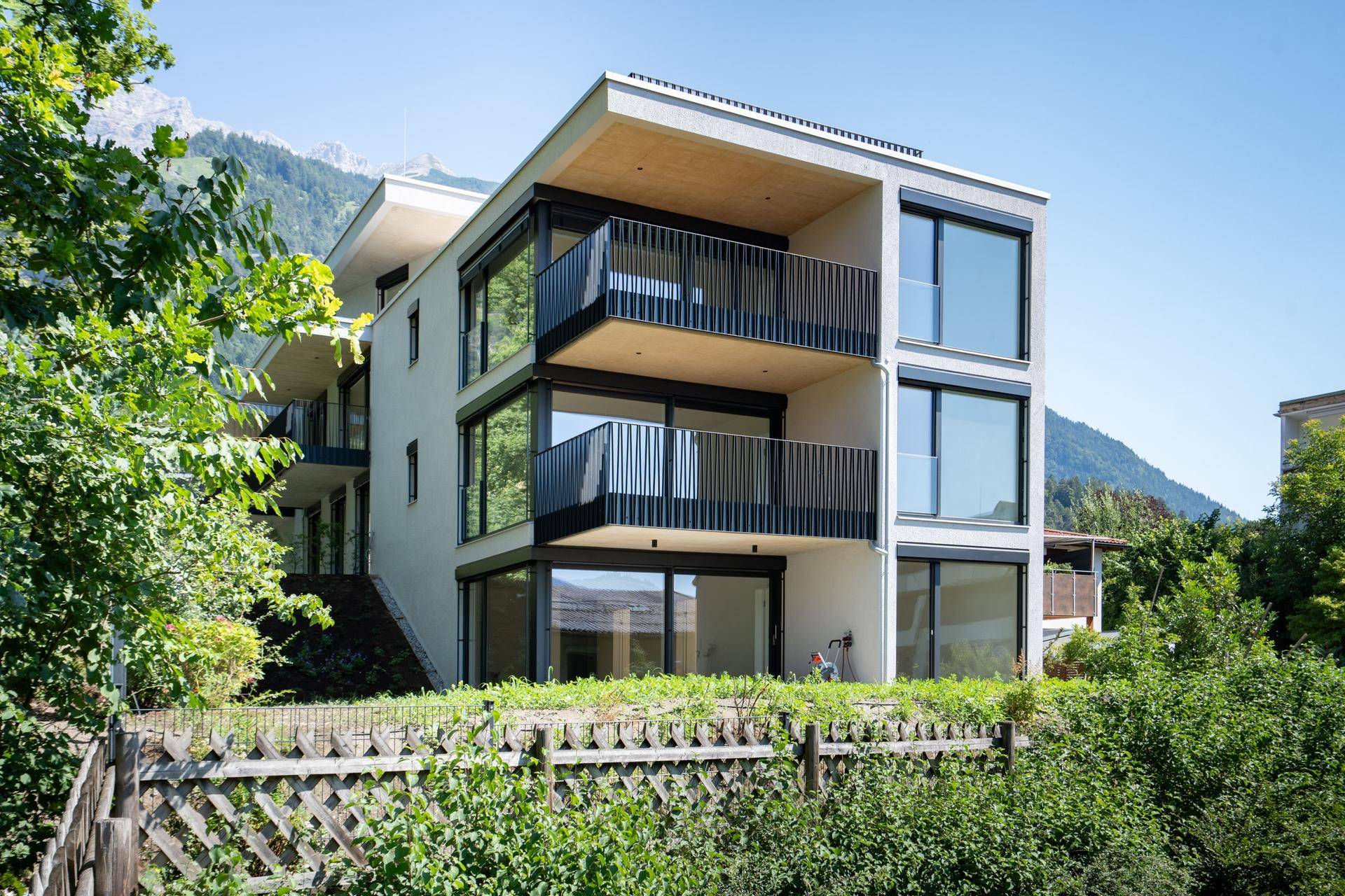 Moderne Wohnanlage mit mehreren Balkonen und Bergblick in grüner Umgebung.