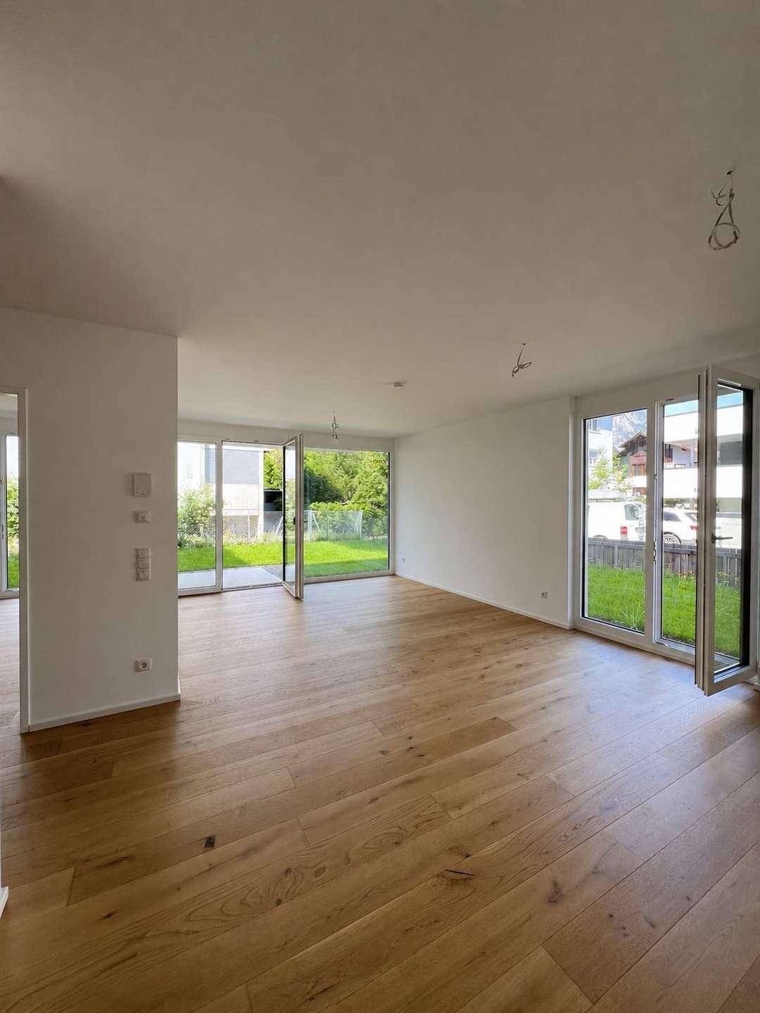 Heller, leerer Wohnbereich mit Eichenparkett und großen Fenstern zum Garten.