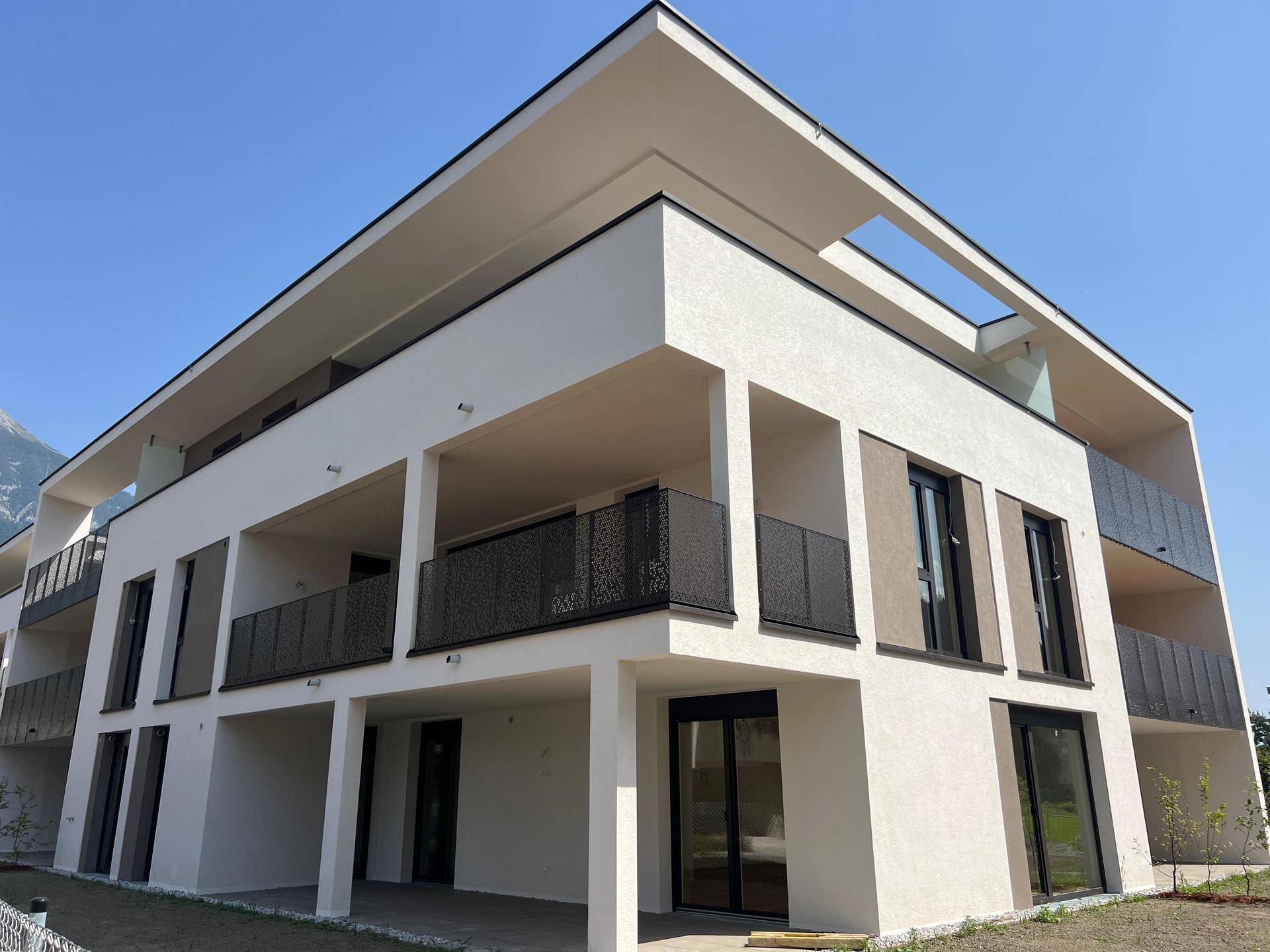 Moderne Architektur eines Mehrfamilienhauses mit Balkonen und großen Fenstern vor alpiner Kulisse.